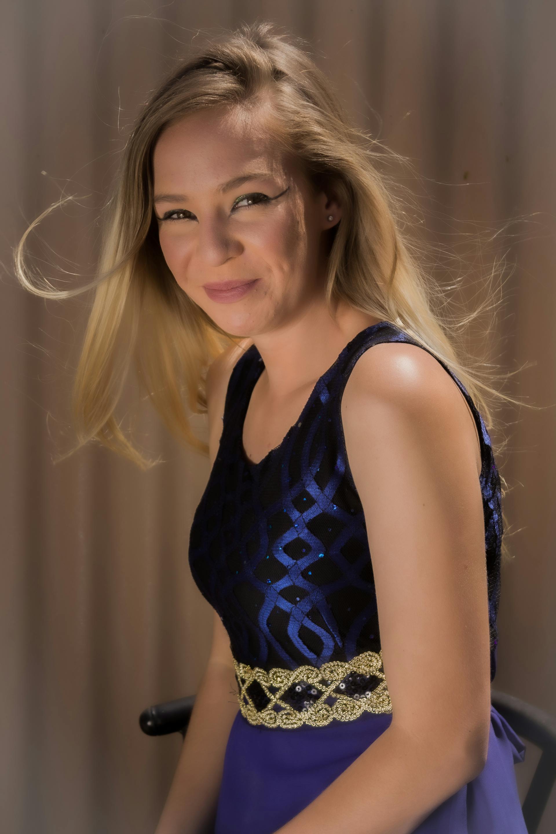 A beautiful young woman with blonde hair smiling while wearing a sparkly blue and gold dress | Source: Pexels