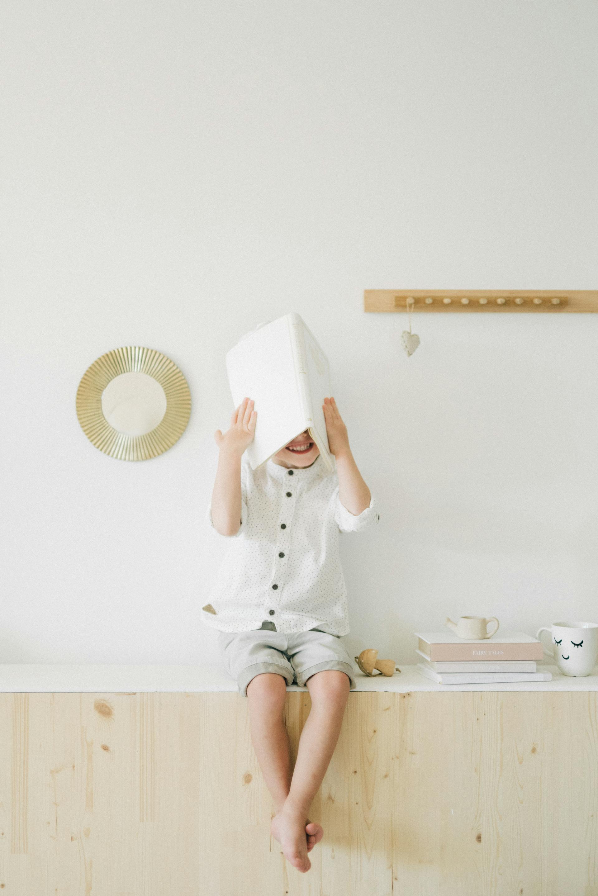 A young boy covering his face with a book | Source: Pexels