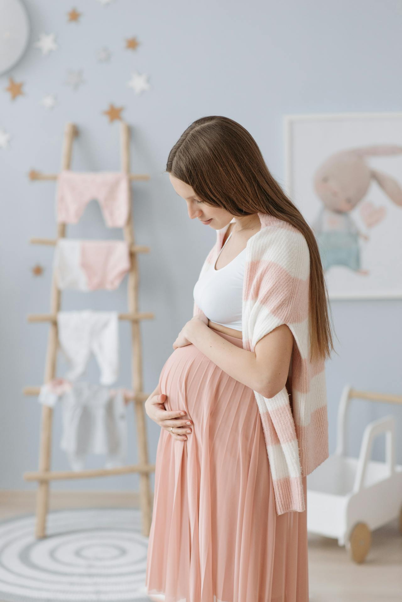 A pregnant woman rubbing her baby bump while standing in a nursery painted in a pale blue shade | Source: Pexels