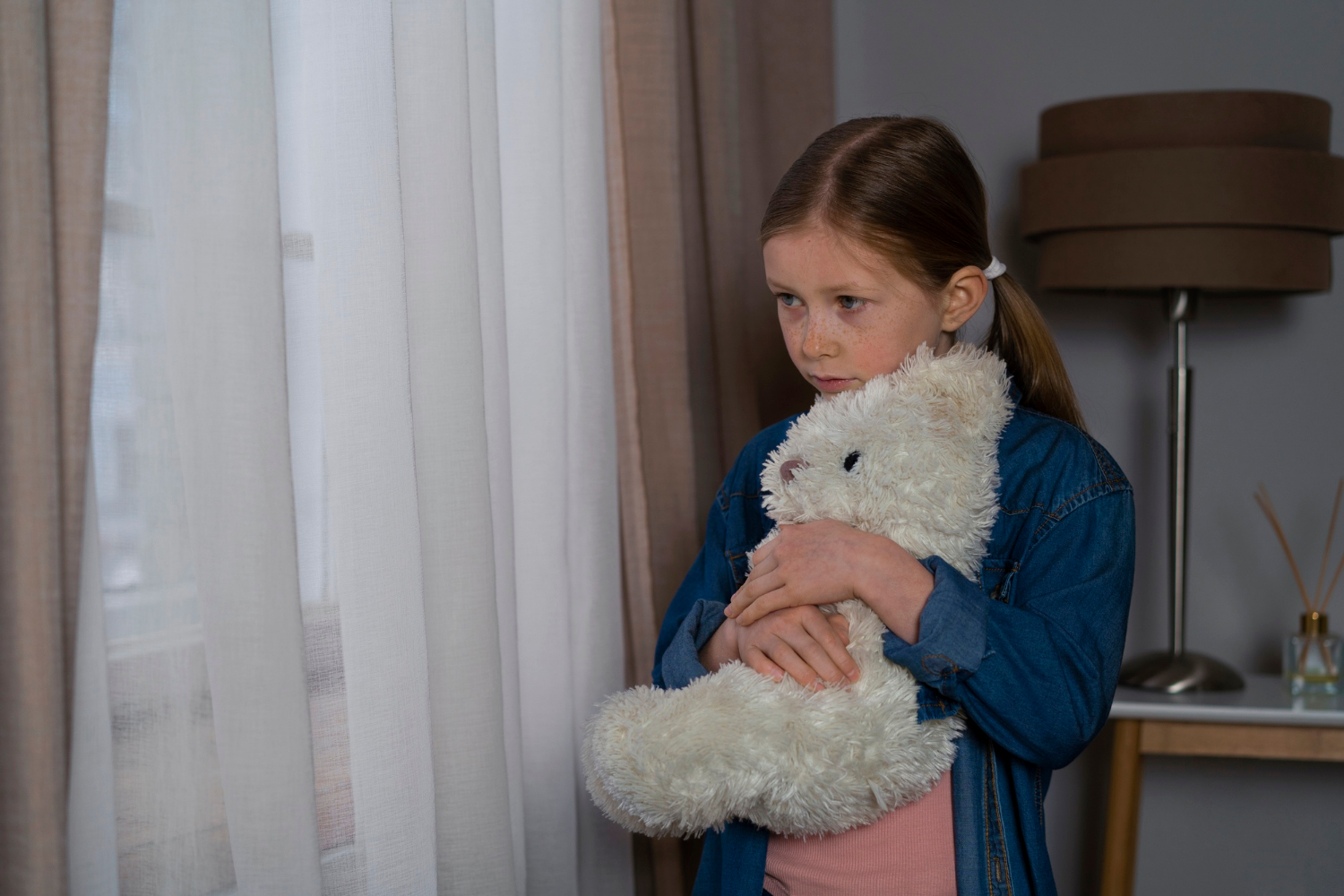 A sad young girl holding a teddy bear | Source: Freepik