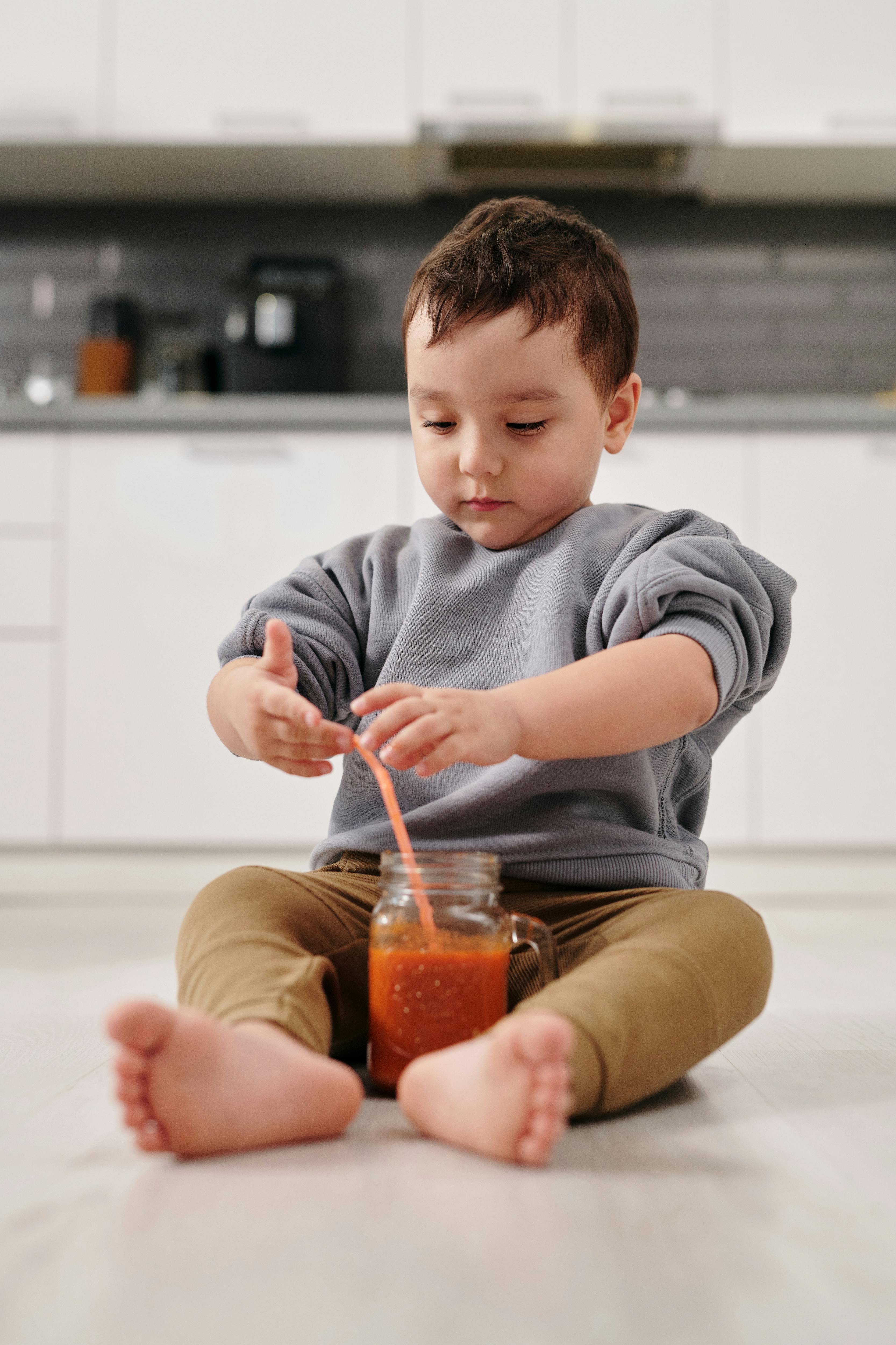 A child sitting on the floor beside a glass of juice with a straw | Source: Pexels