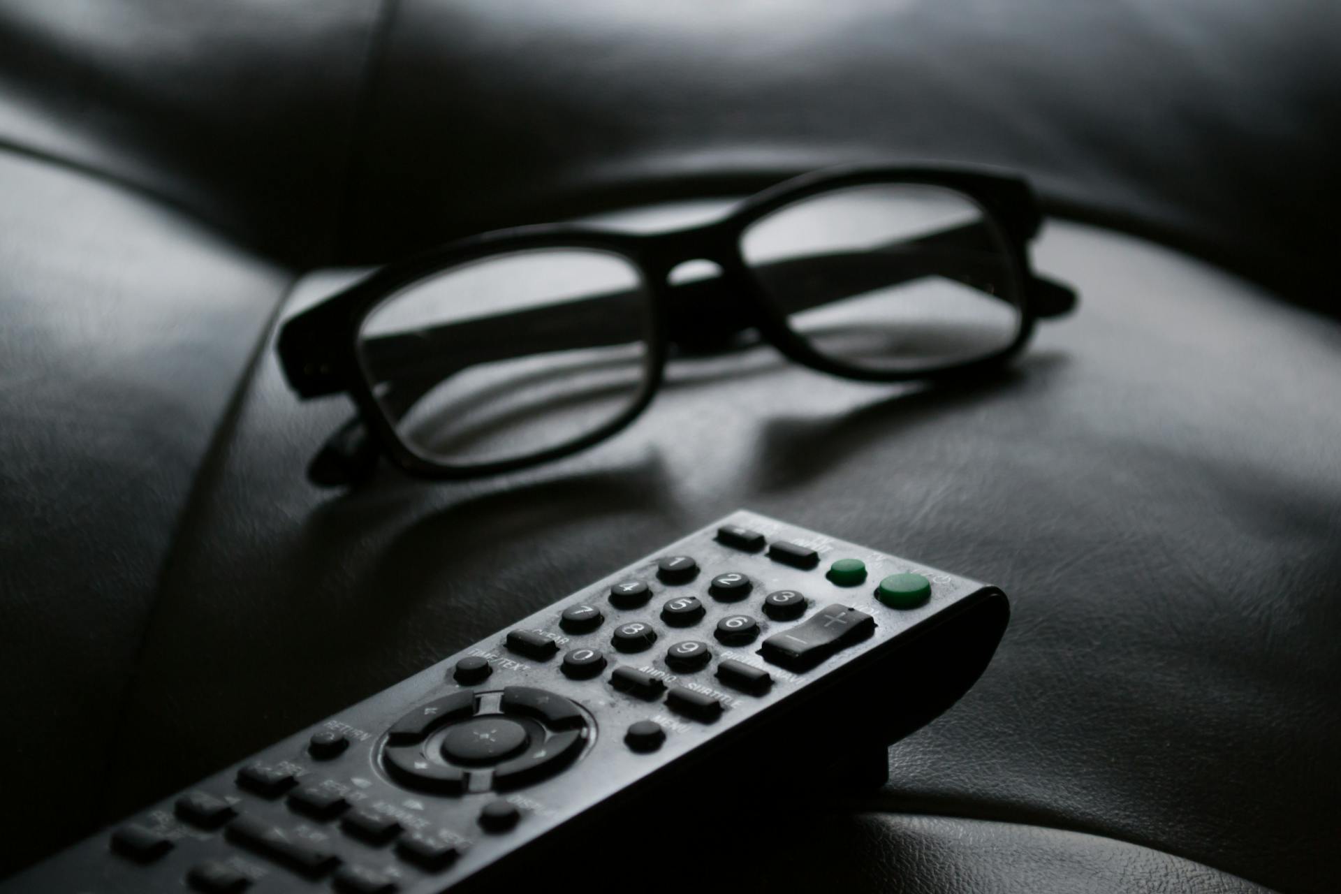 A grayscale photo of a remote control near eyeglasses | Source: Pexels