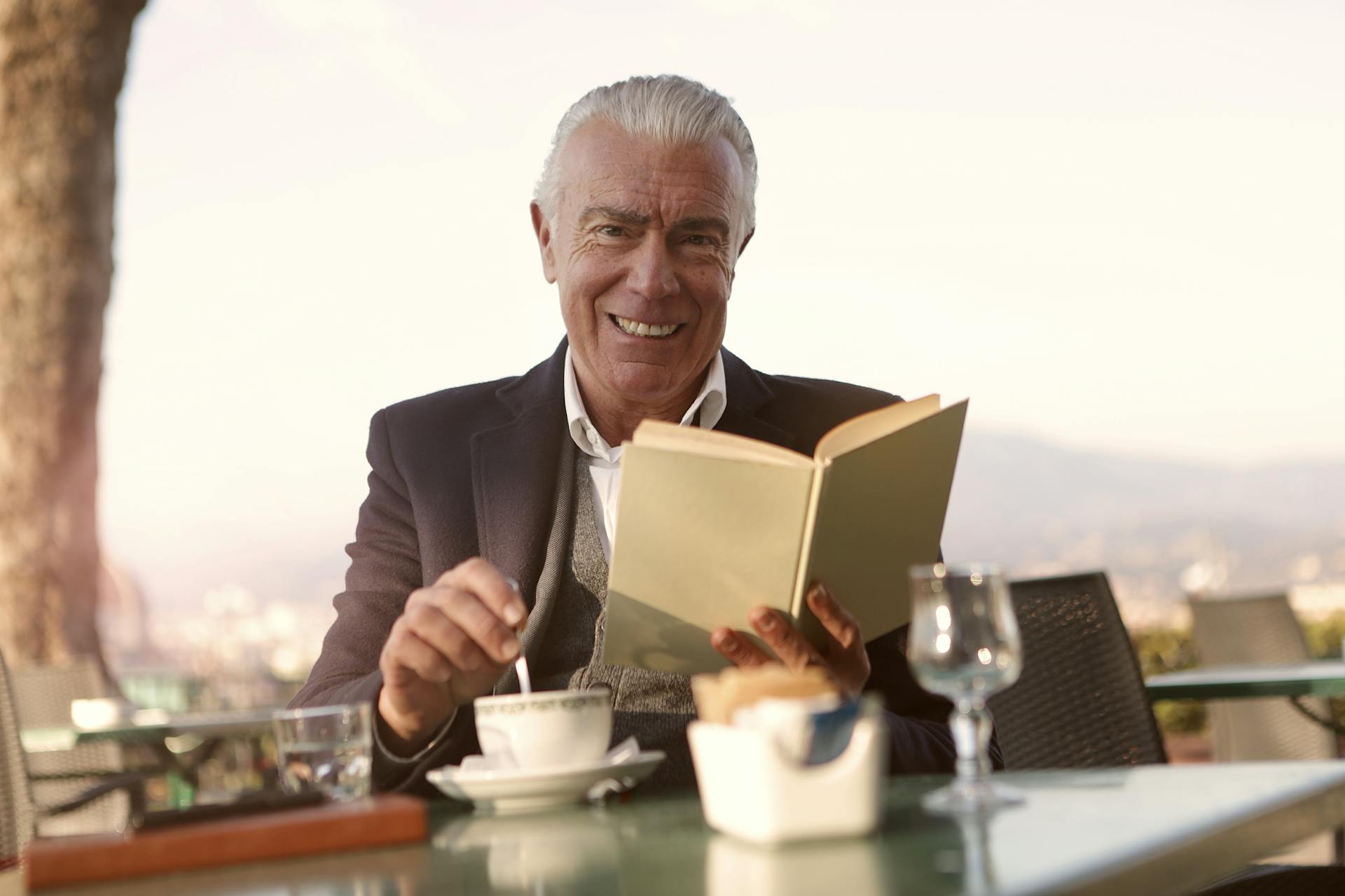 A man seated at a table and smiling while holding a book | Source: Pexels