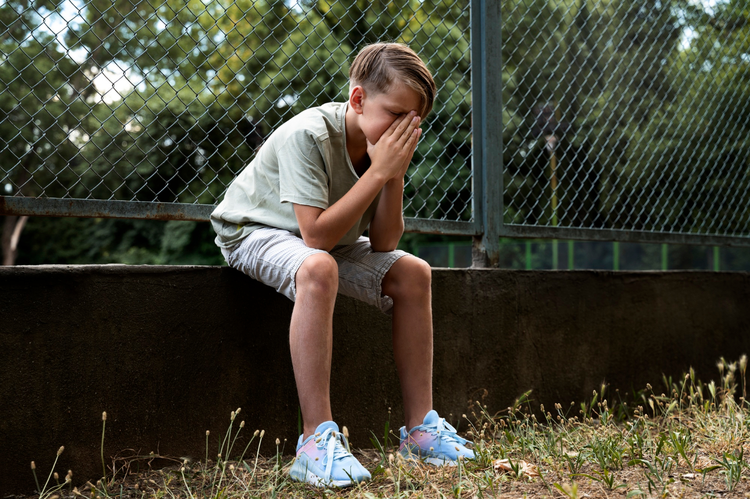 A heartbroken boy sitting on a low-built fence wall | Source: Freepik