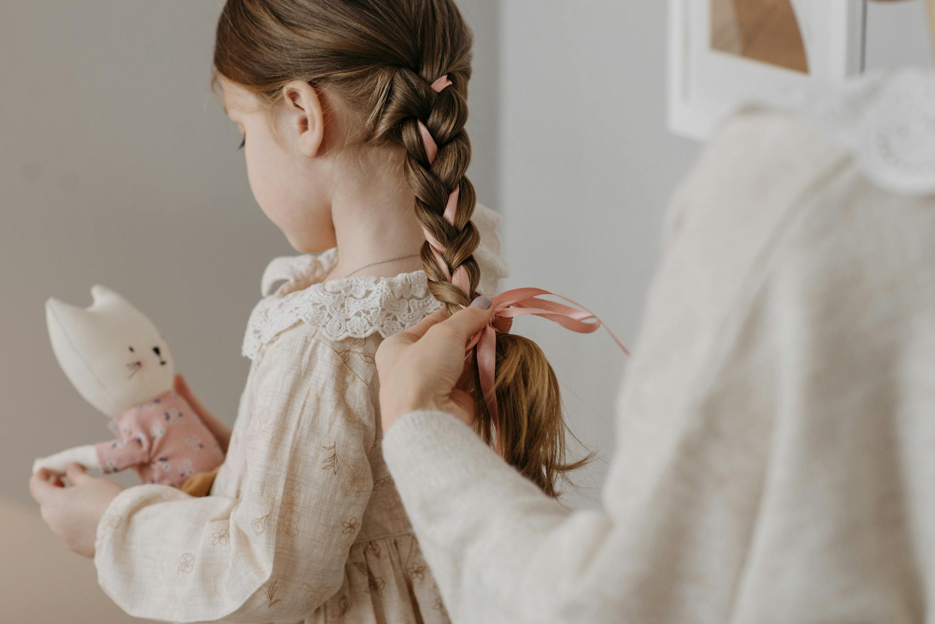 A woman tying a ribbon on her daughter's hair | Source: Pexels