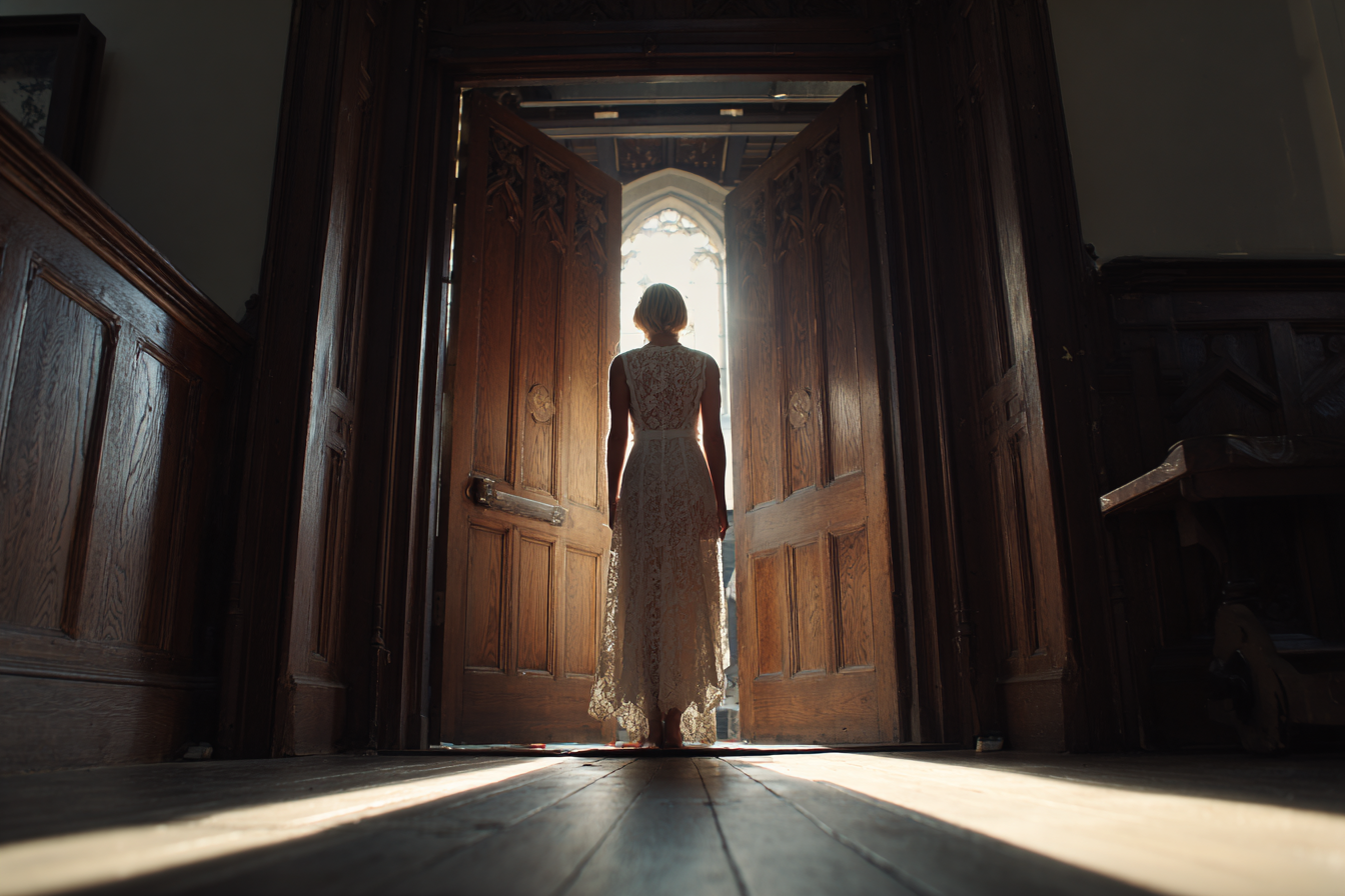 A woman wearing a white lace dress standing in a doorway | Source: Midjourney
