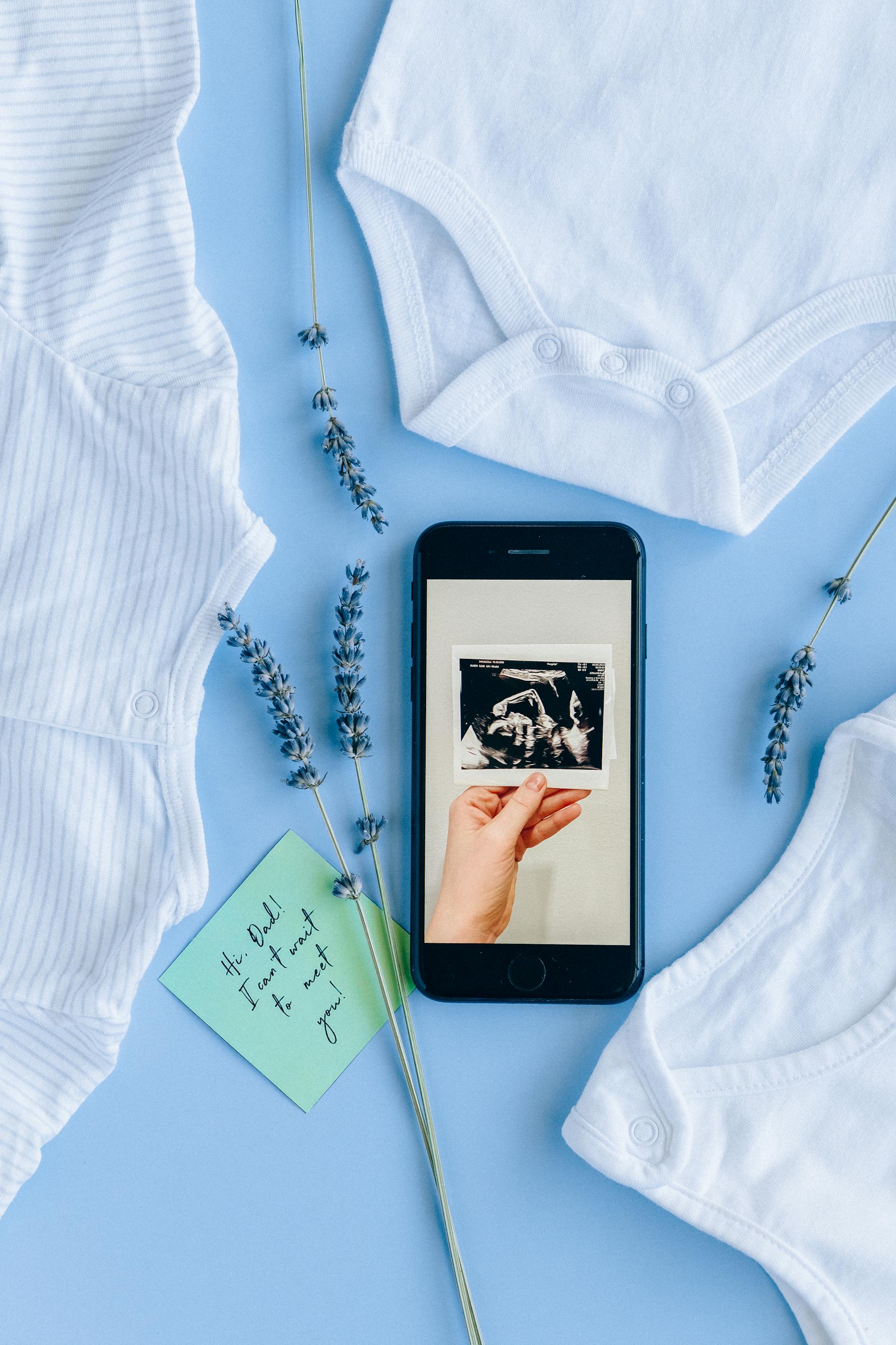 A sonogram on a phone screen beside baby clothes | Source: Pexels