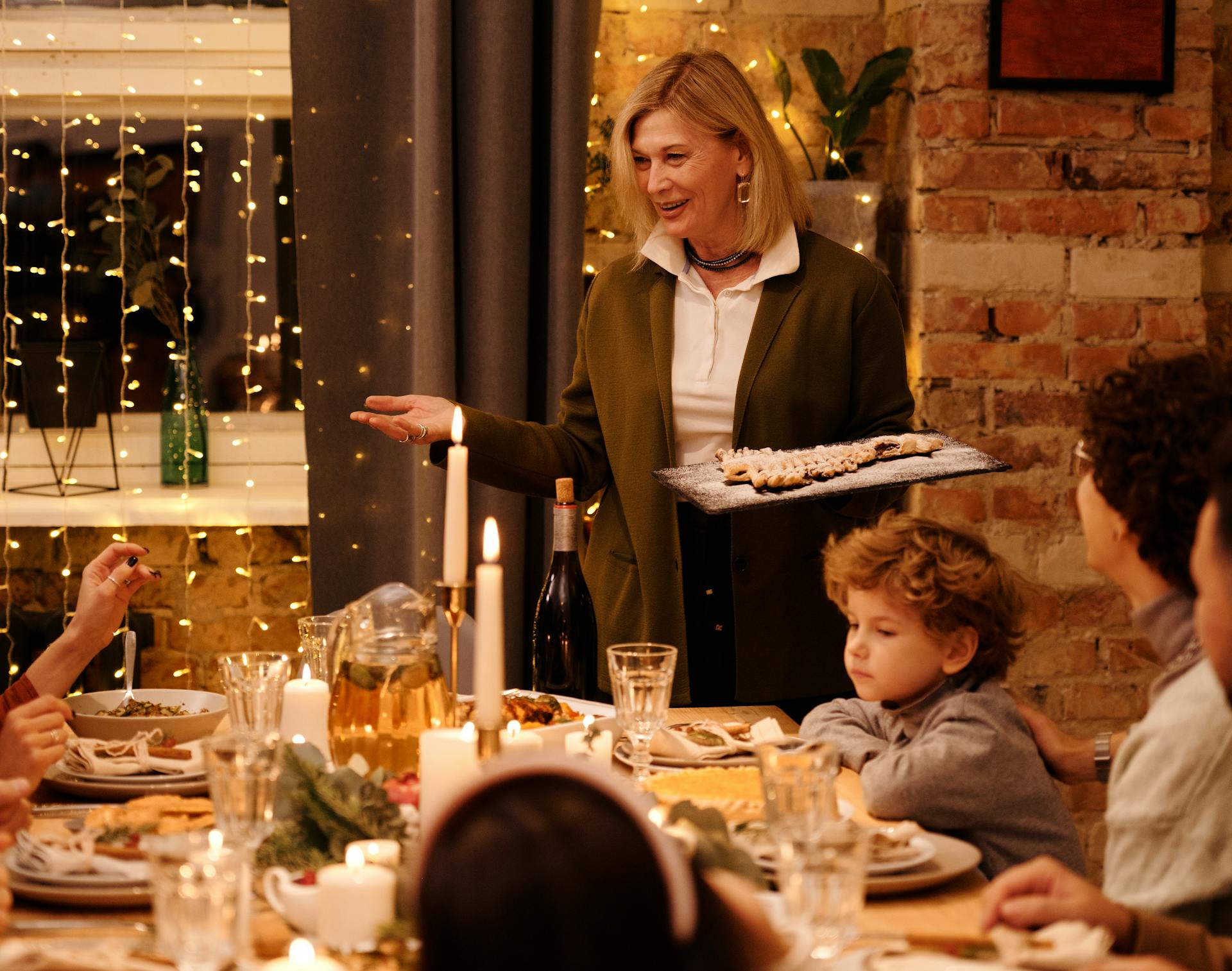 A woman serving food to her family at a dining table with candles and string lights | Source: Pexels