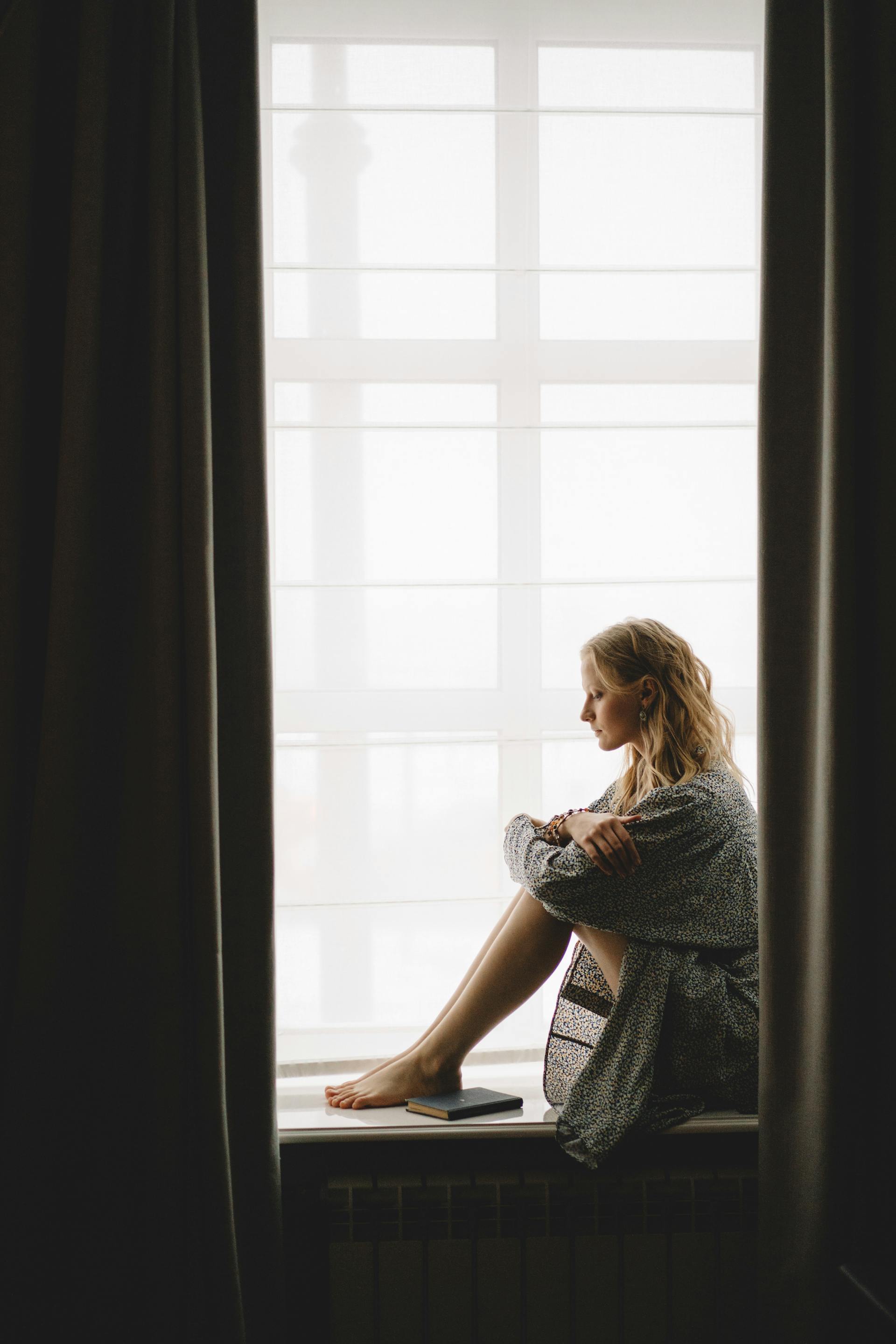 A thoughtful woman sitting on the windowsill | Source: Pexels