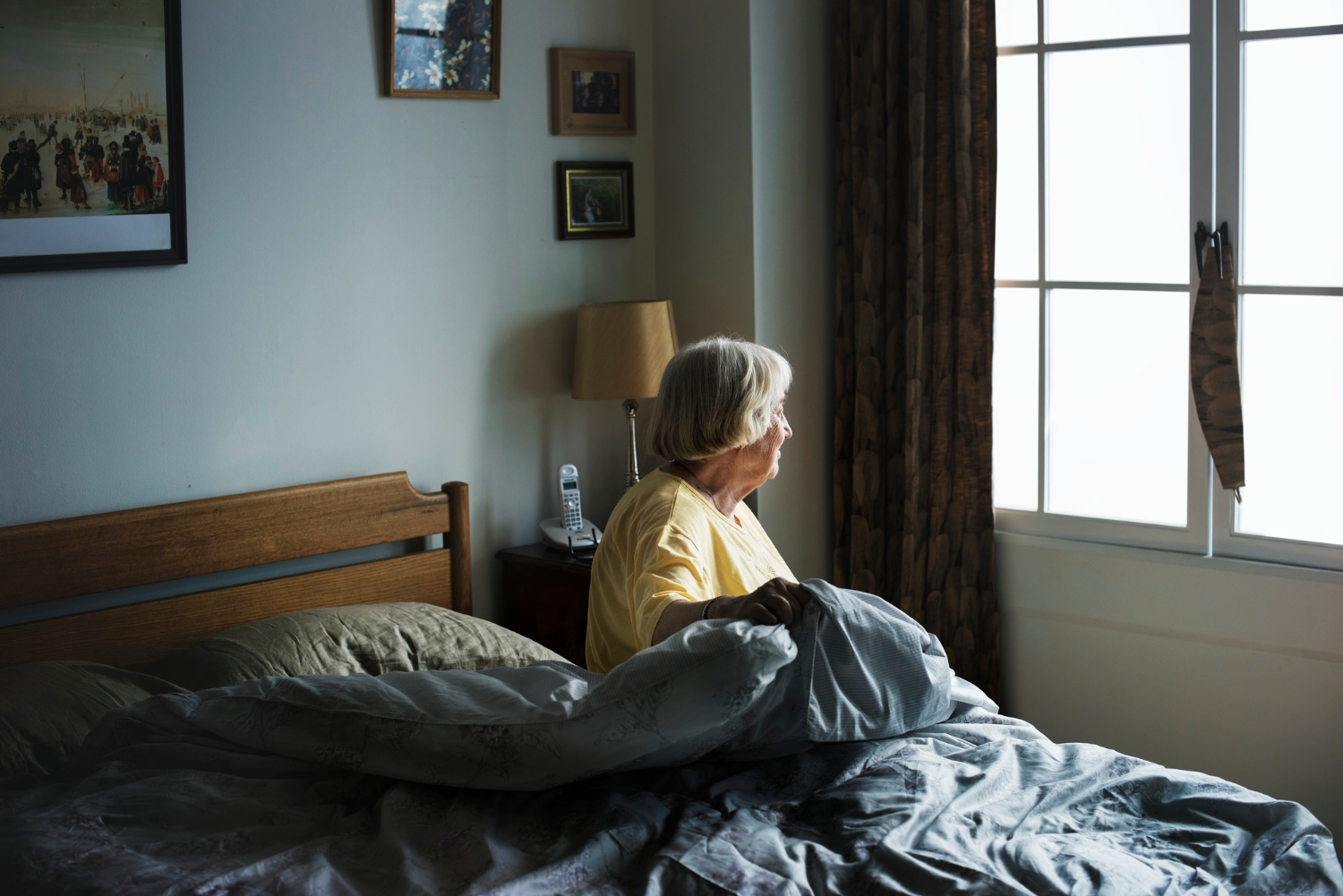 A lonely senior woman sitting on her bed and staring out the window | Source: Freepik