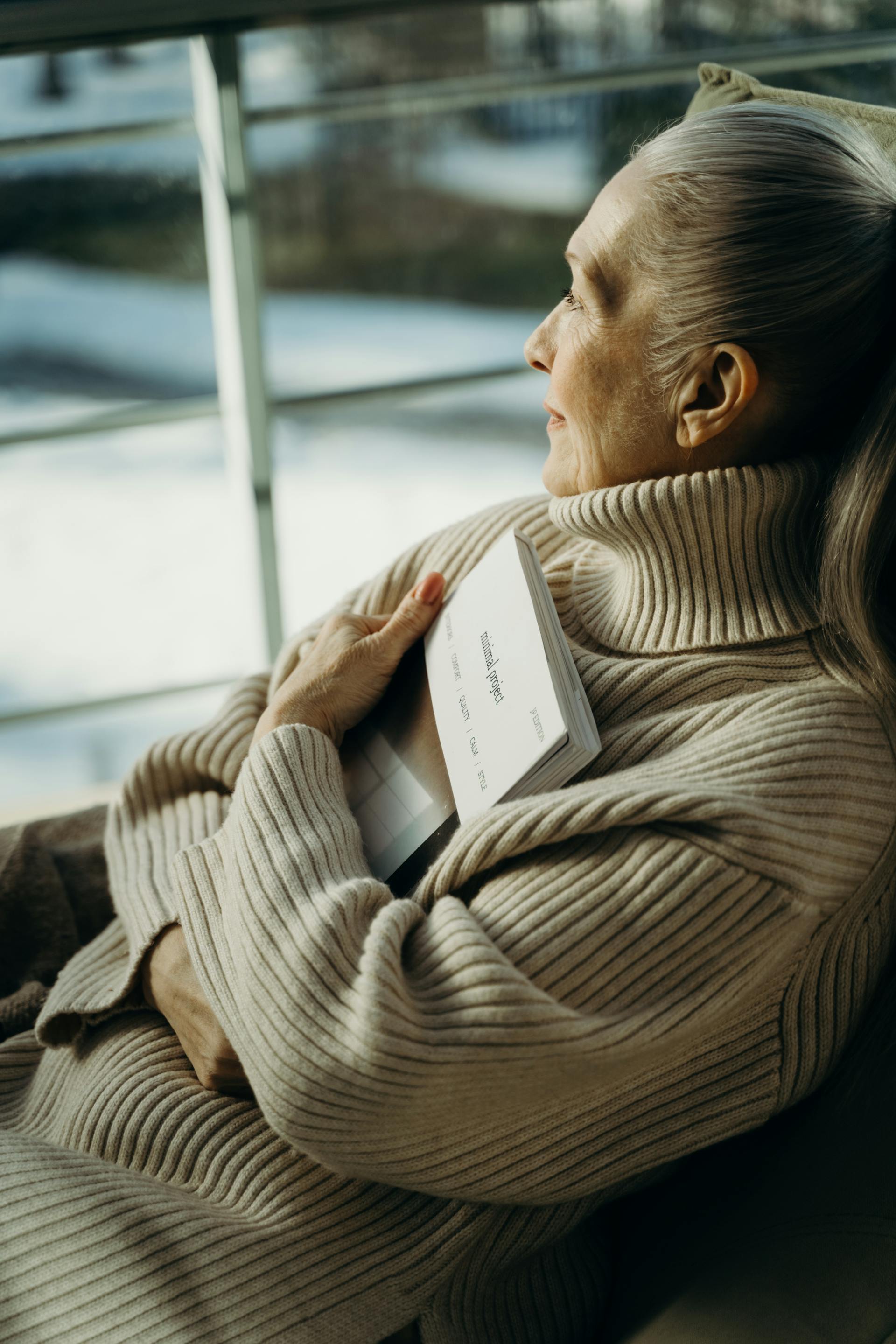 A woman looking out a window while holding a book | Source: Pexels