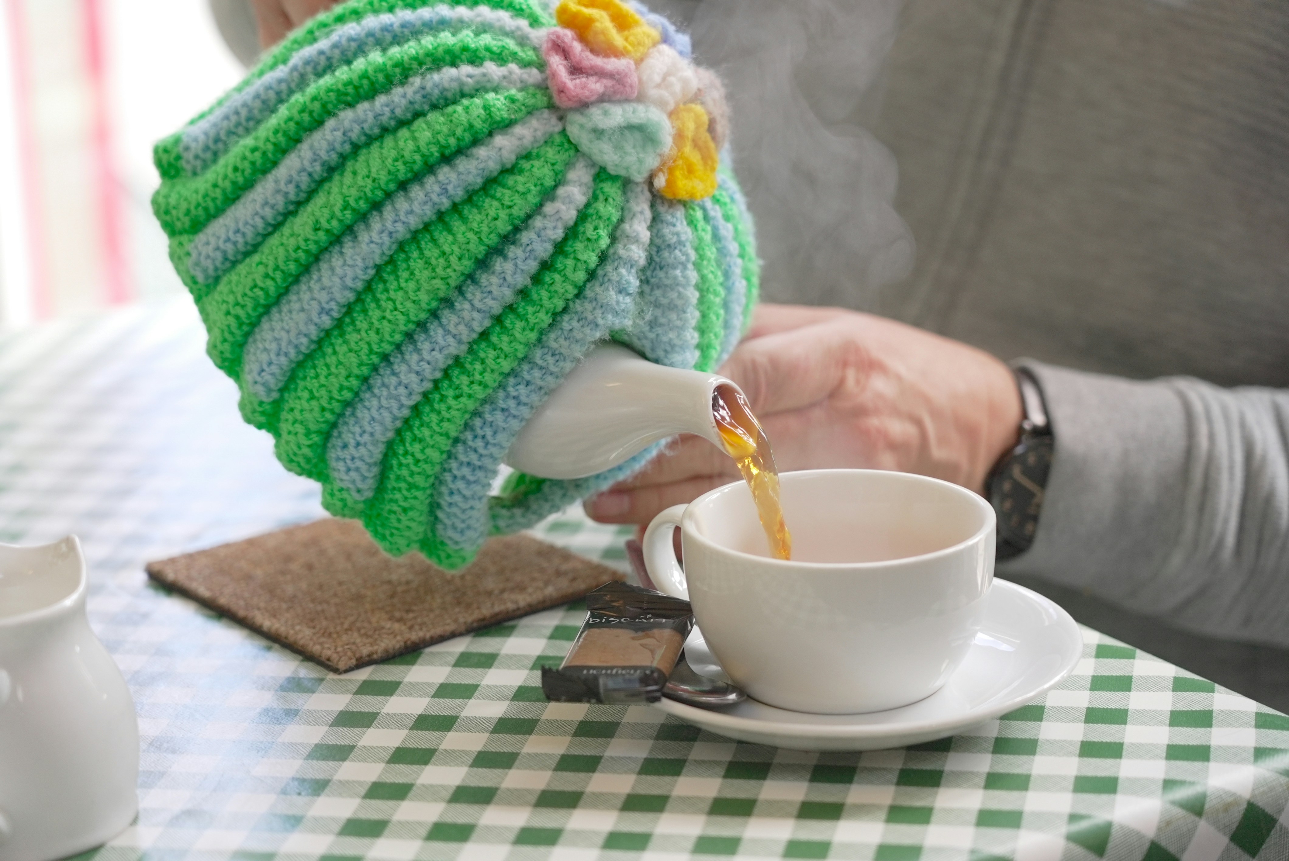 Someone pouring tea with a kettle in a knitted cozy | Source: Unsplash