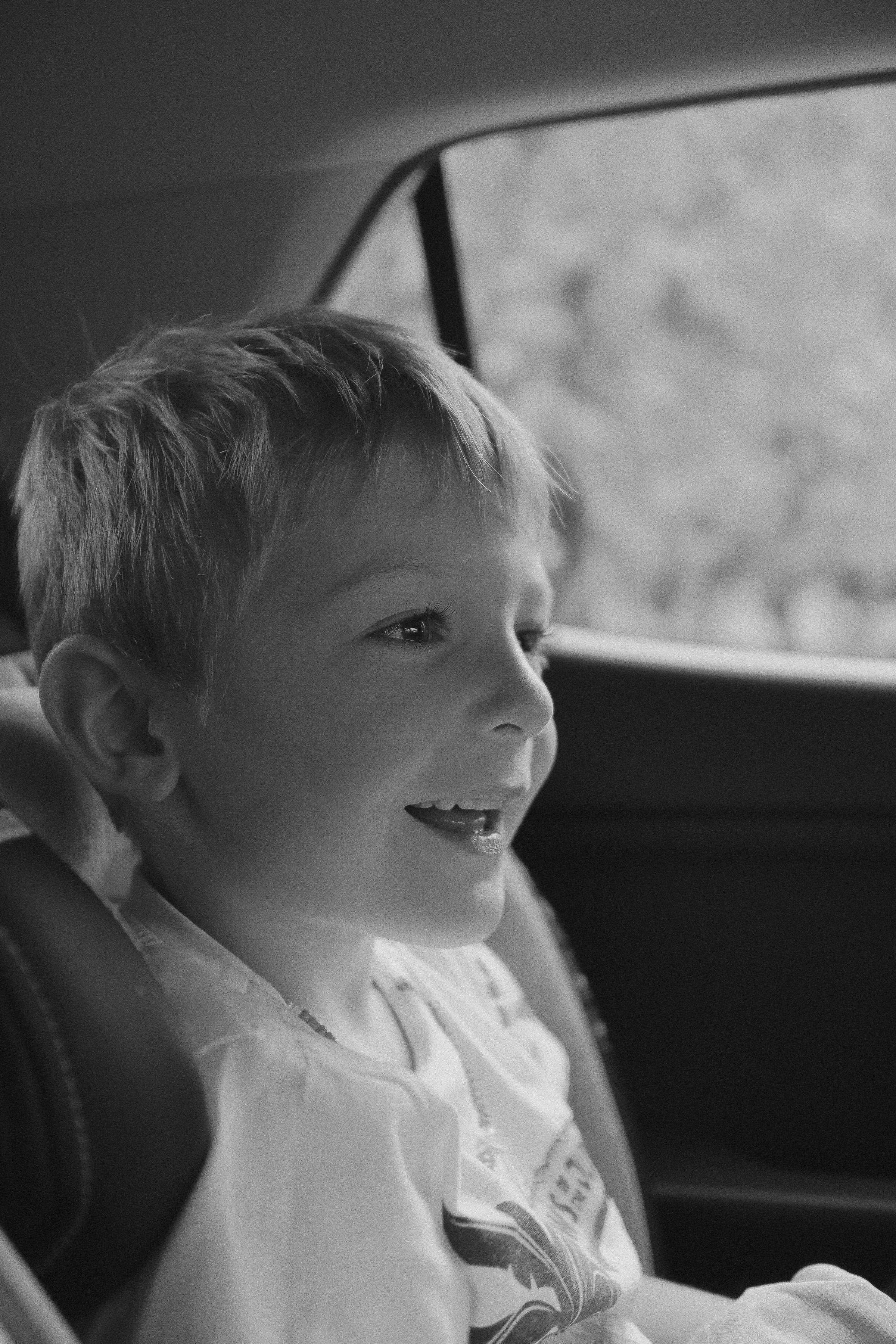 A grayscale photo of a young boy sitting in the backseat of a car | Source: Unsplash