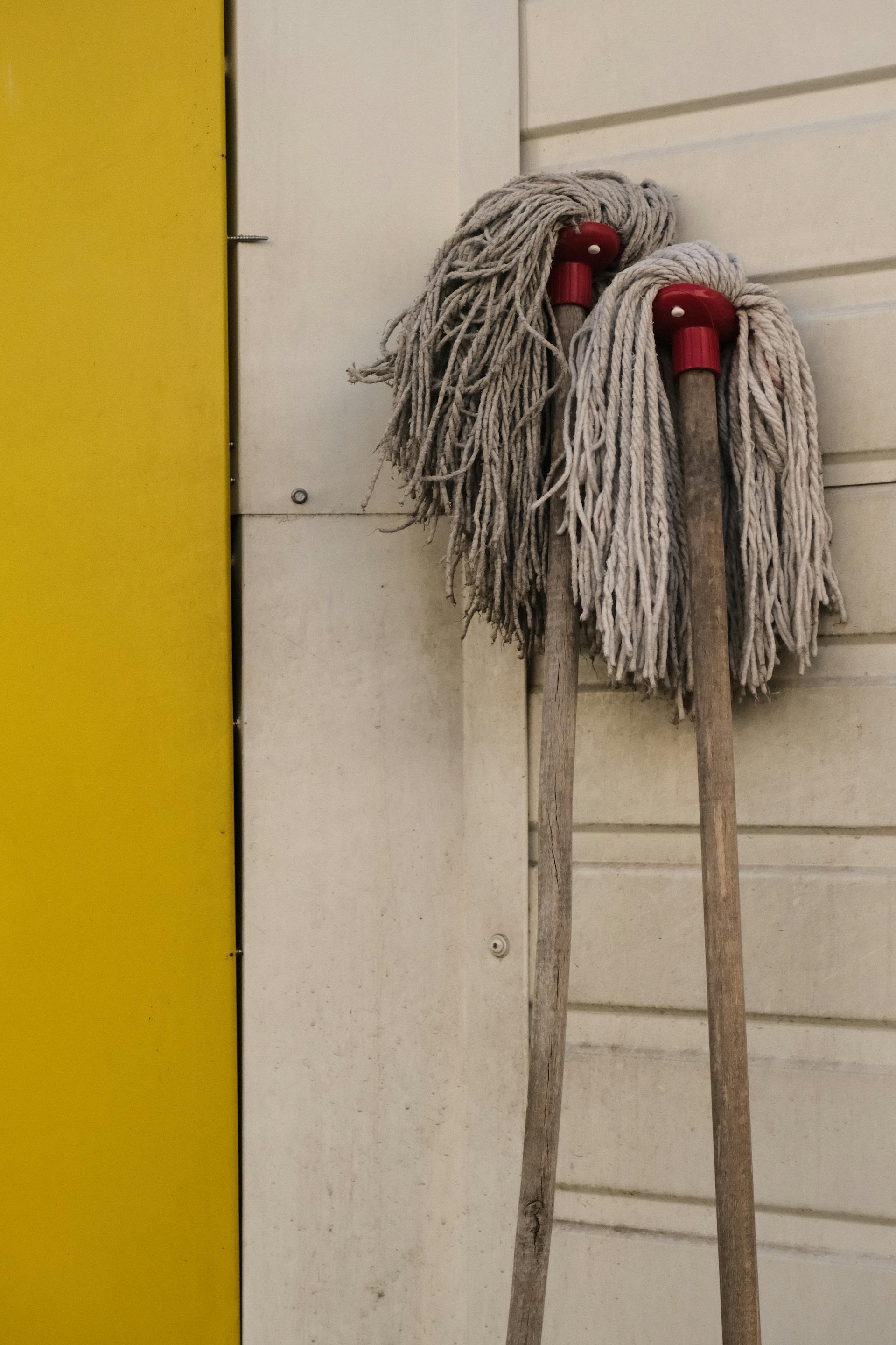 Two worn out mops leaning on a wall | Source: Pexels