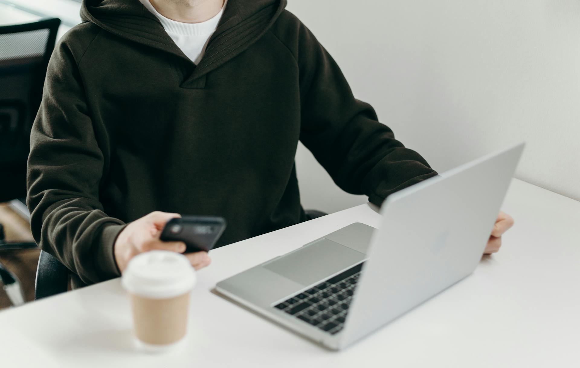 A close-up photo of a young man using his phone while working on his laptop | Source: Pexels