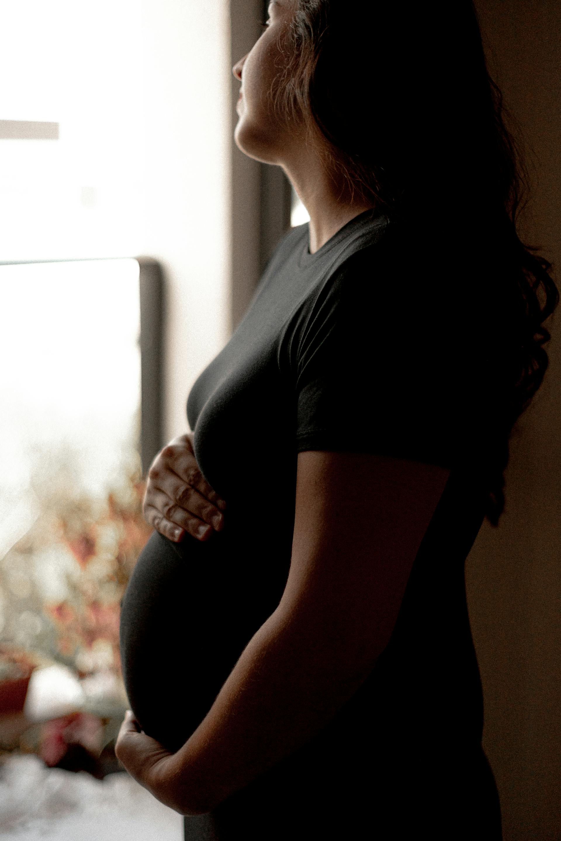 A pregnant woman staring thoughtfully out a window | Source: Pexels