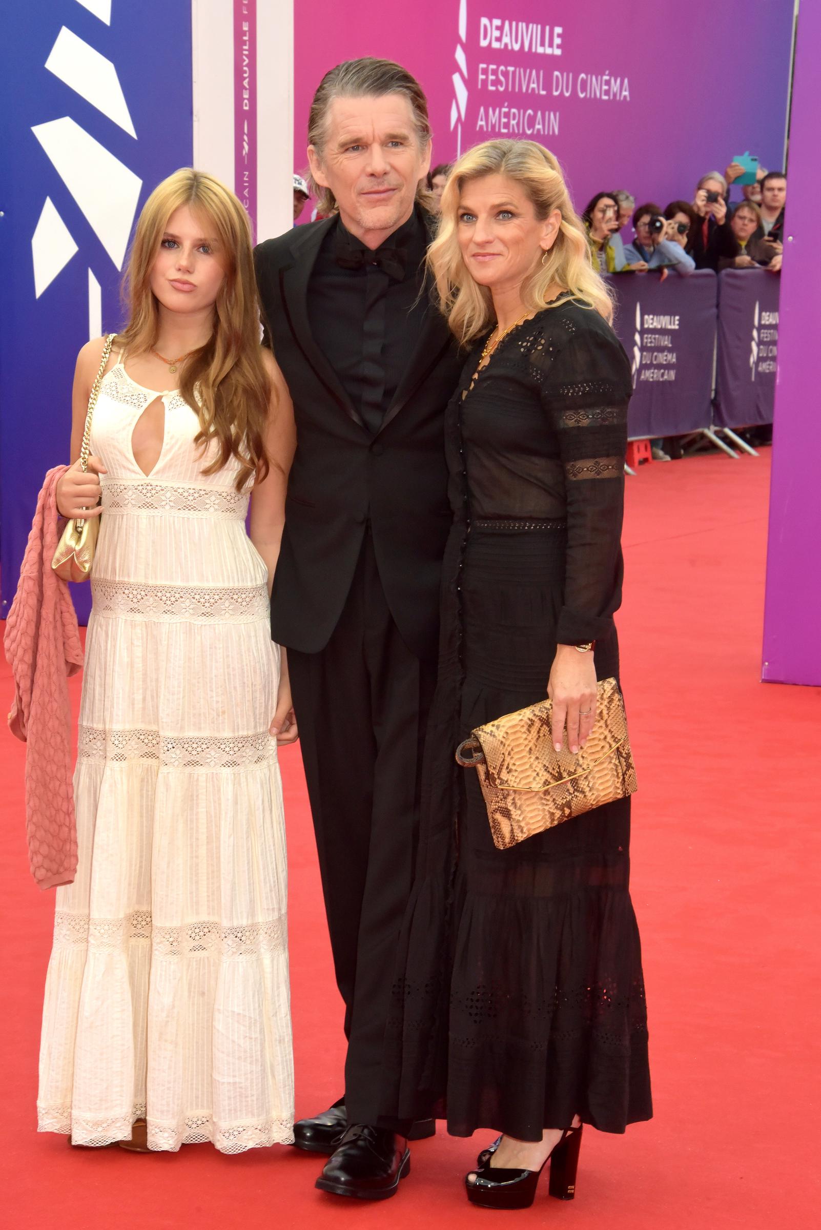 Ethan Hawke poses with his wife, Ryan Hawke, and their daughter, Indiana Hawke, at the Deauville American Film Festival in Deauville, France, on September 4, 2026. Ethan wore a black tuxedo, while Ryan opted for a long black dress and Indiana stood out in a white dress with lace-like detailing and a pink garment draped over her arm. | Source: Getty Images