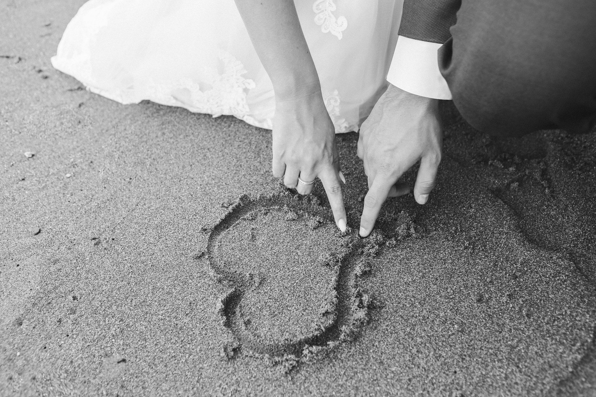 Grayscale shot of a couple drawing a heart on the sand | Source: Unsplash