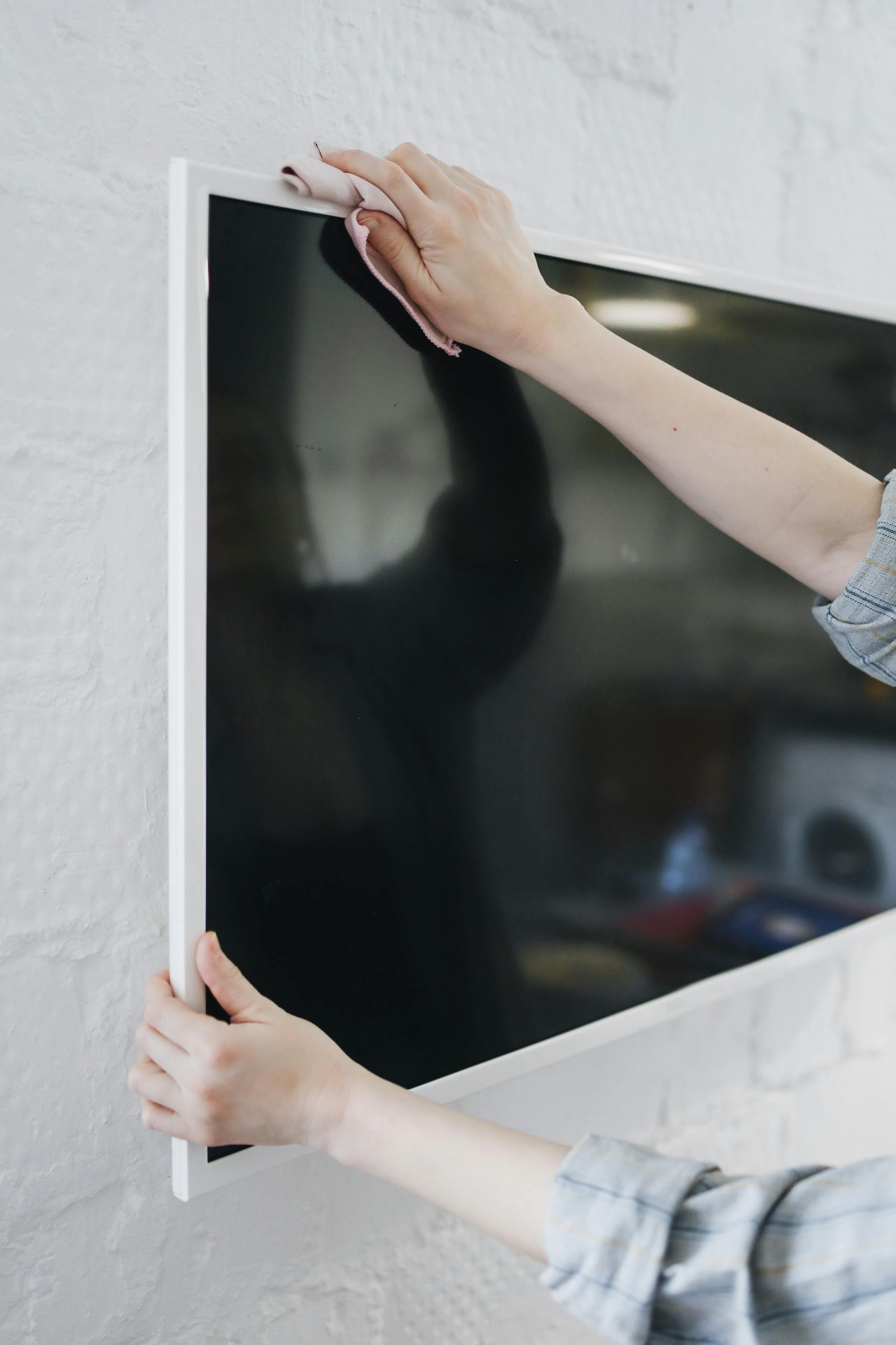 A close-up of a person wiping a television mounted on a wall | Source: Pexels