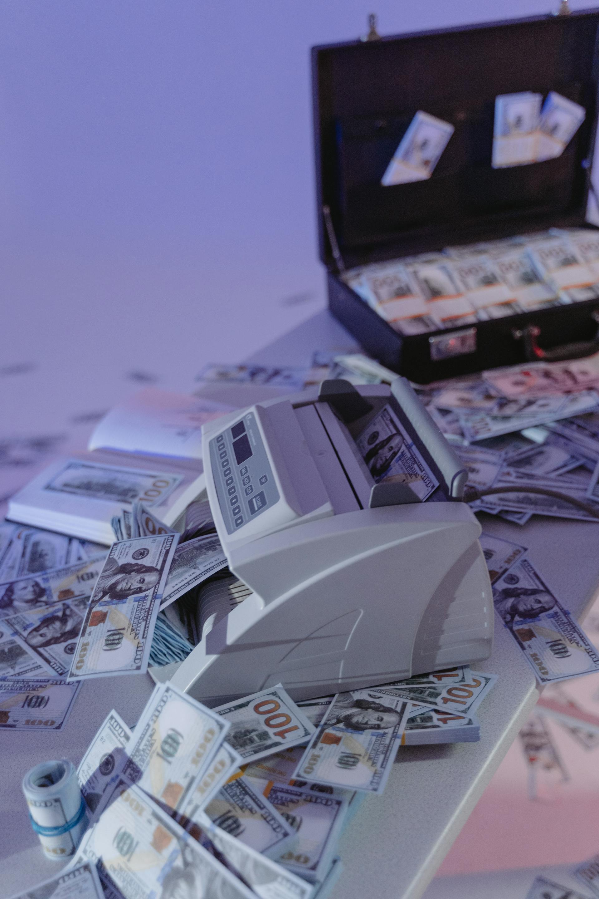 A money counting machine and a suitcase stashed with cash | Source: Pexels