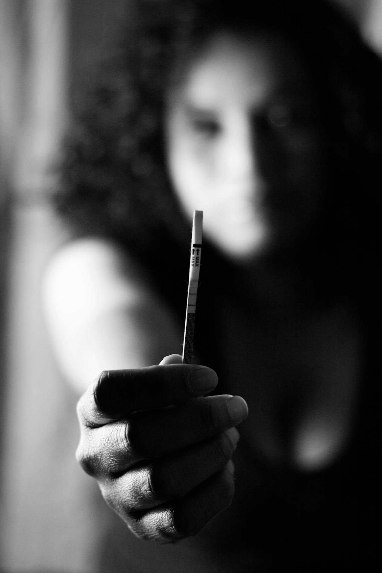 Grayscale shot of a woman holding a pregnancy test in focus | Source: Pexels