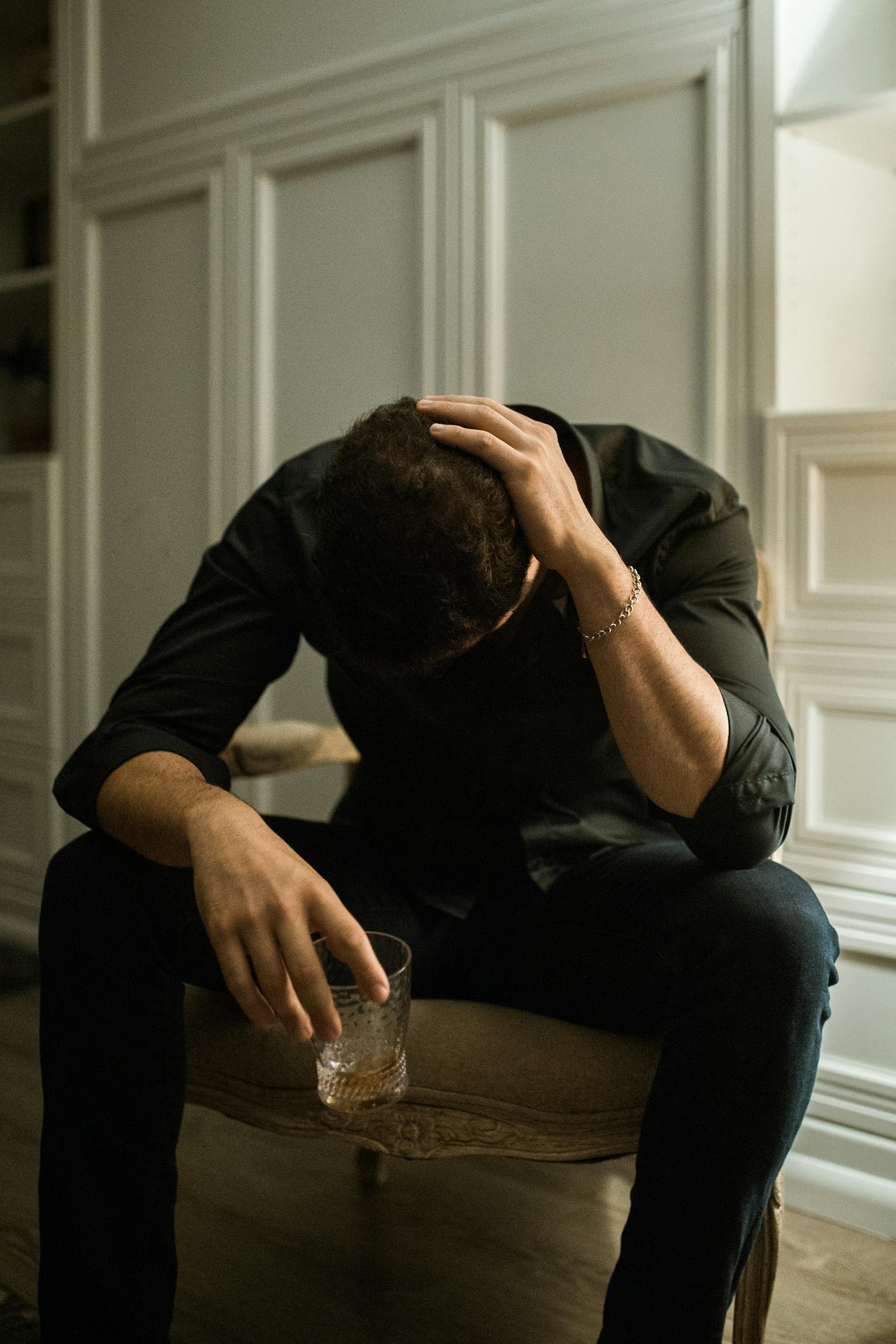 A distressed man sitting with his head bowed down while holding a glass of drink | Source: Pexels