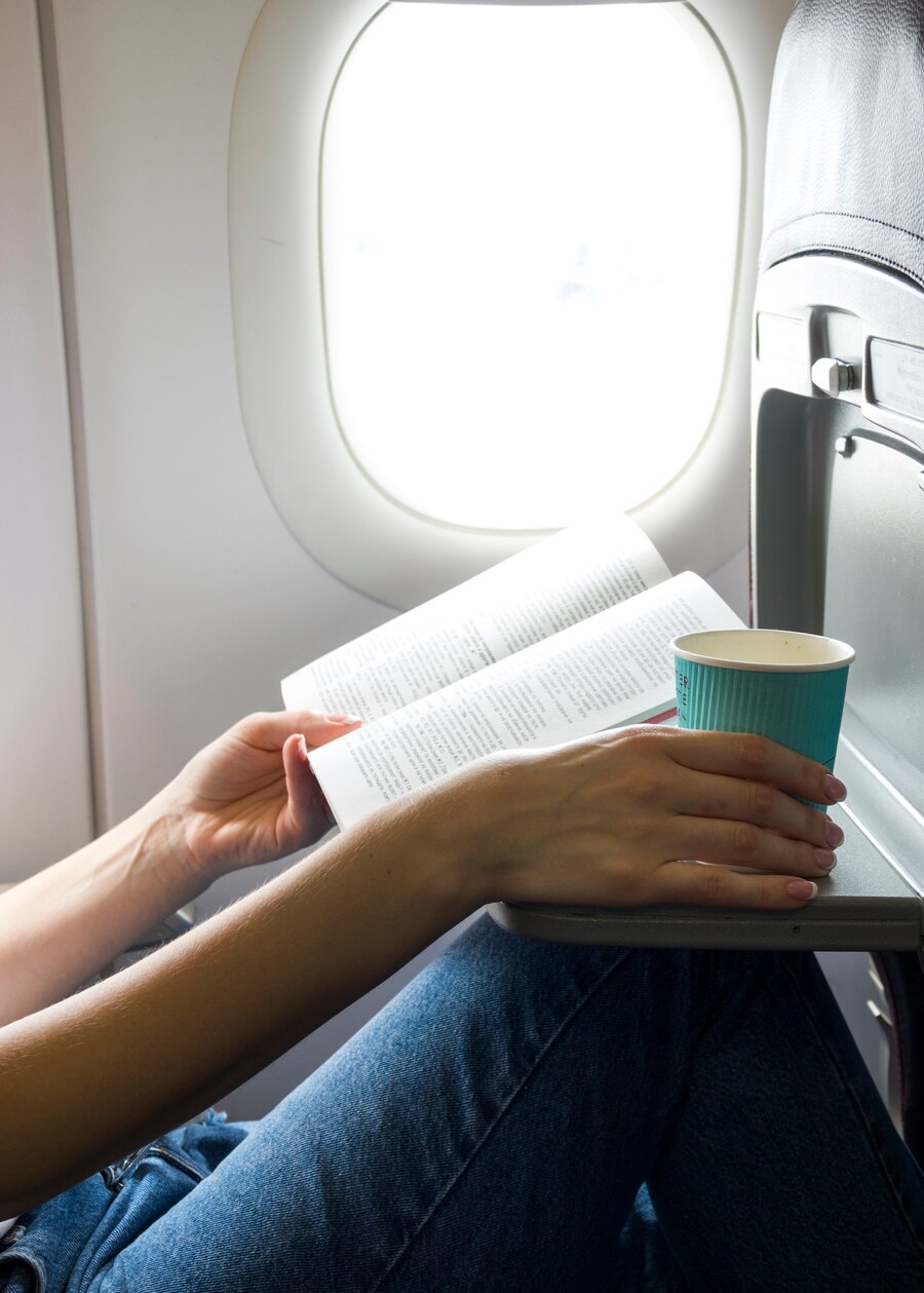 A woman with a book and a coffee in a window seat | Source: Freepik