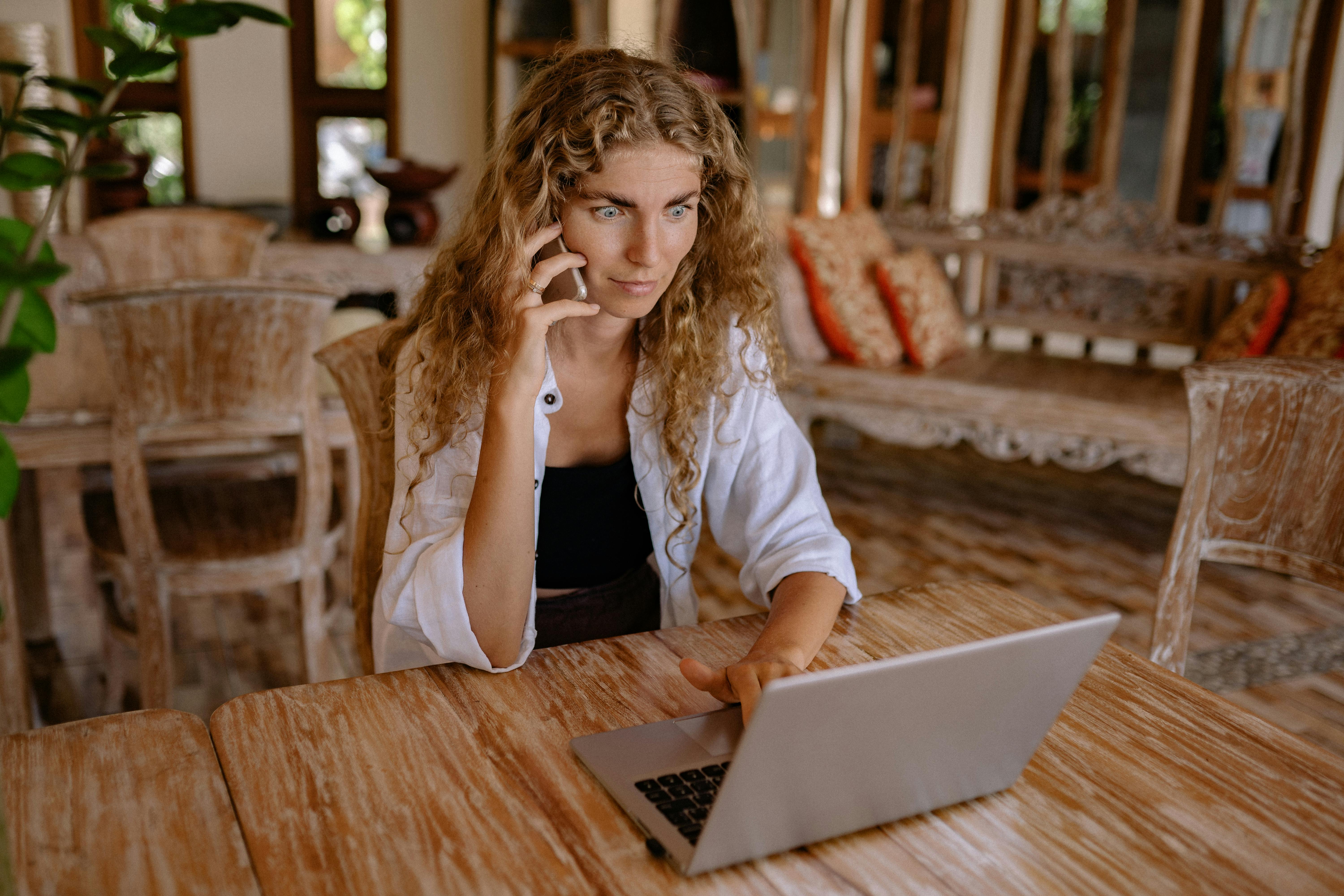 A woman on a phone call while using a laptop | Source: Pexels