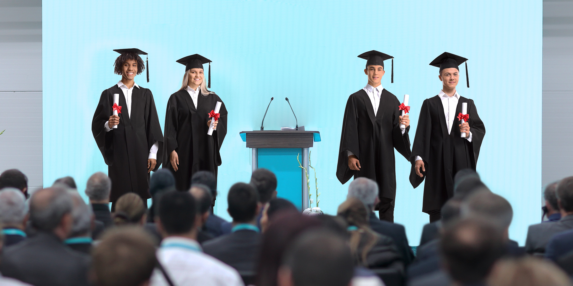 Graduates in caps and gowns proudly hold their diplomas on stage as the audience looks on | Source: Shutterstock