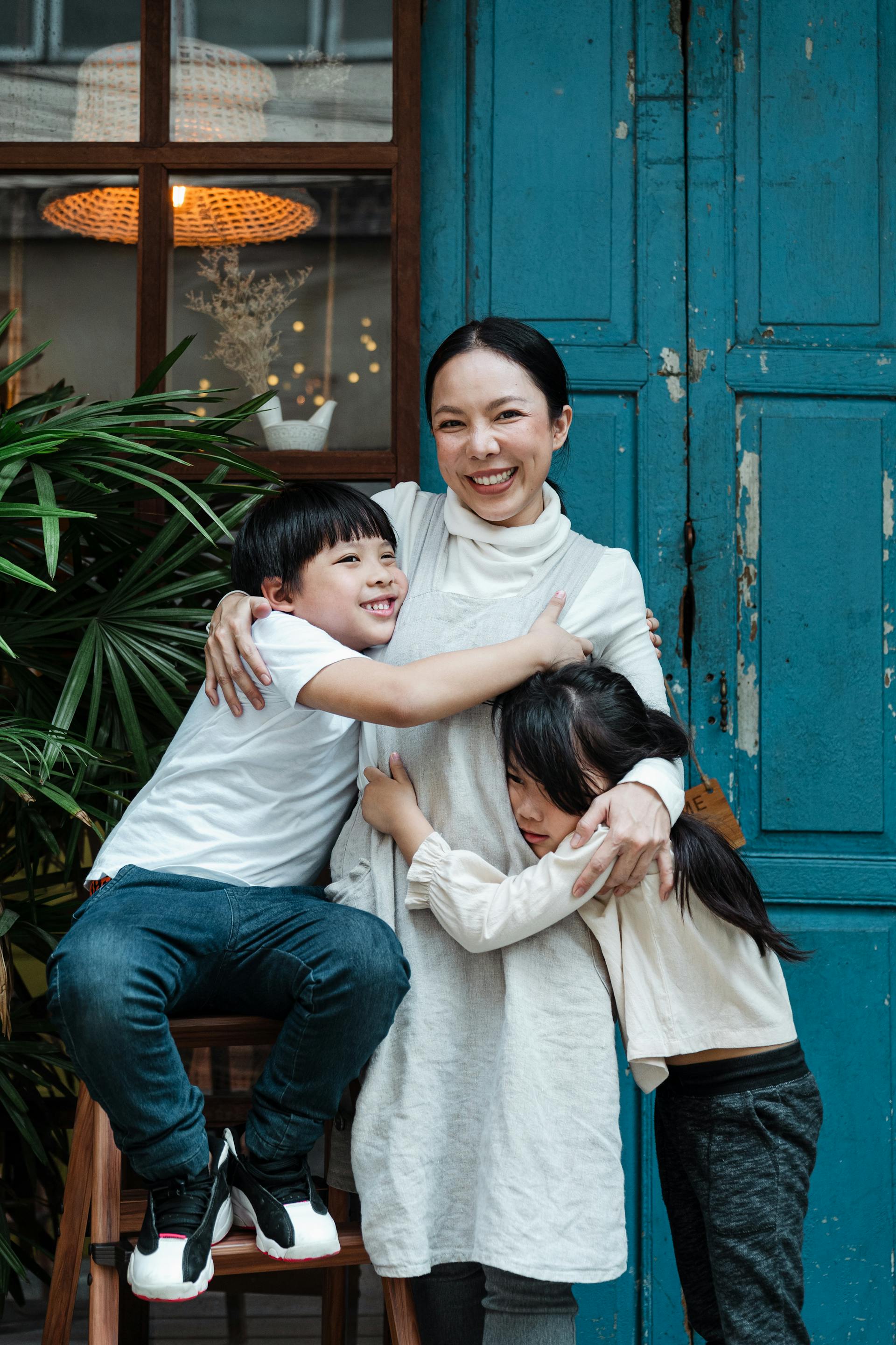 A happy mother embracing her two children while standing in front of a blue door | Source: Pexels