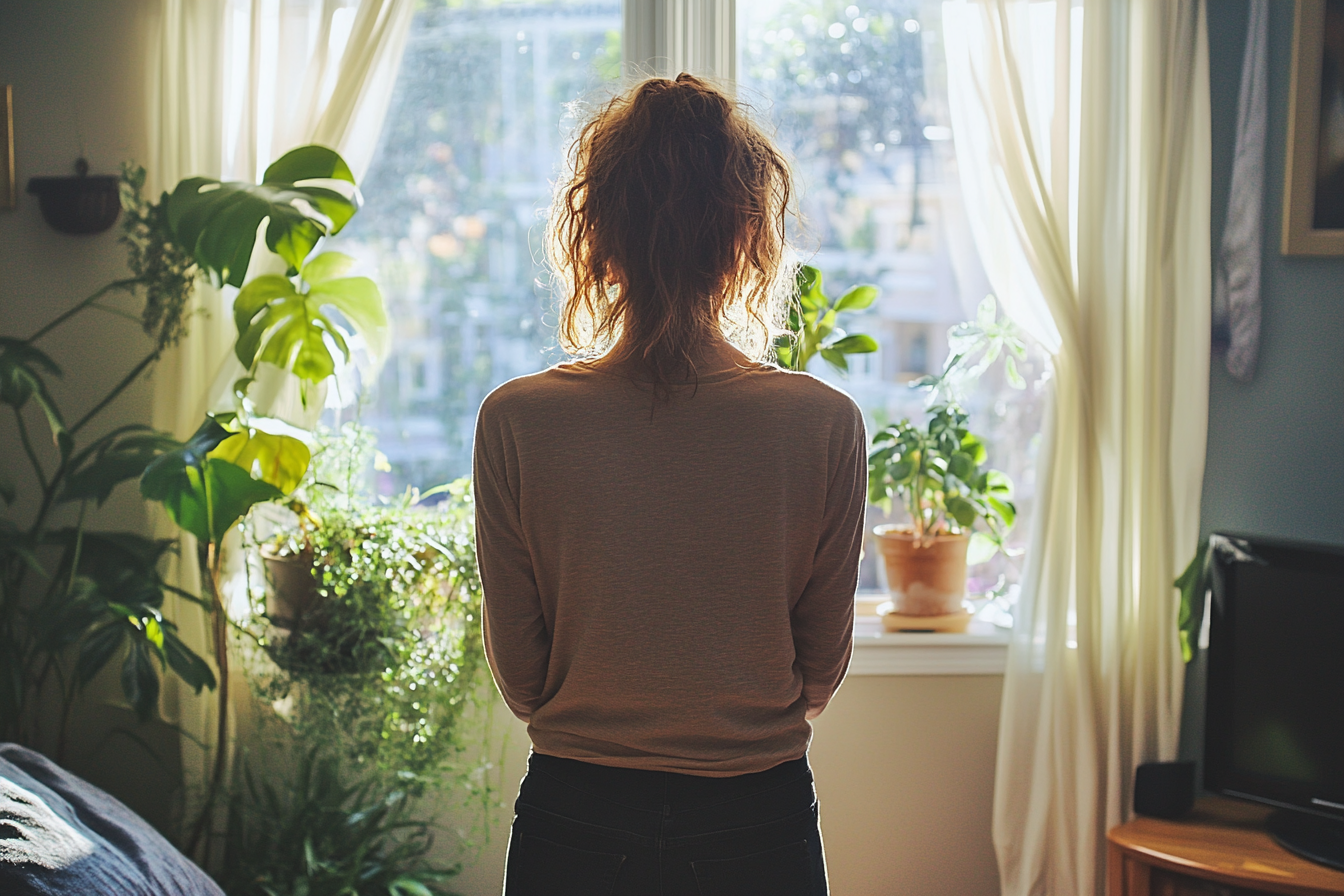 A woman standing near a window | Source: Midjourney