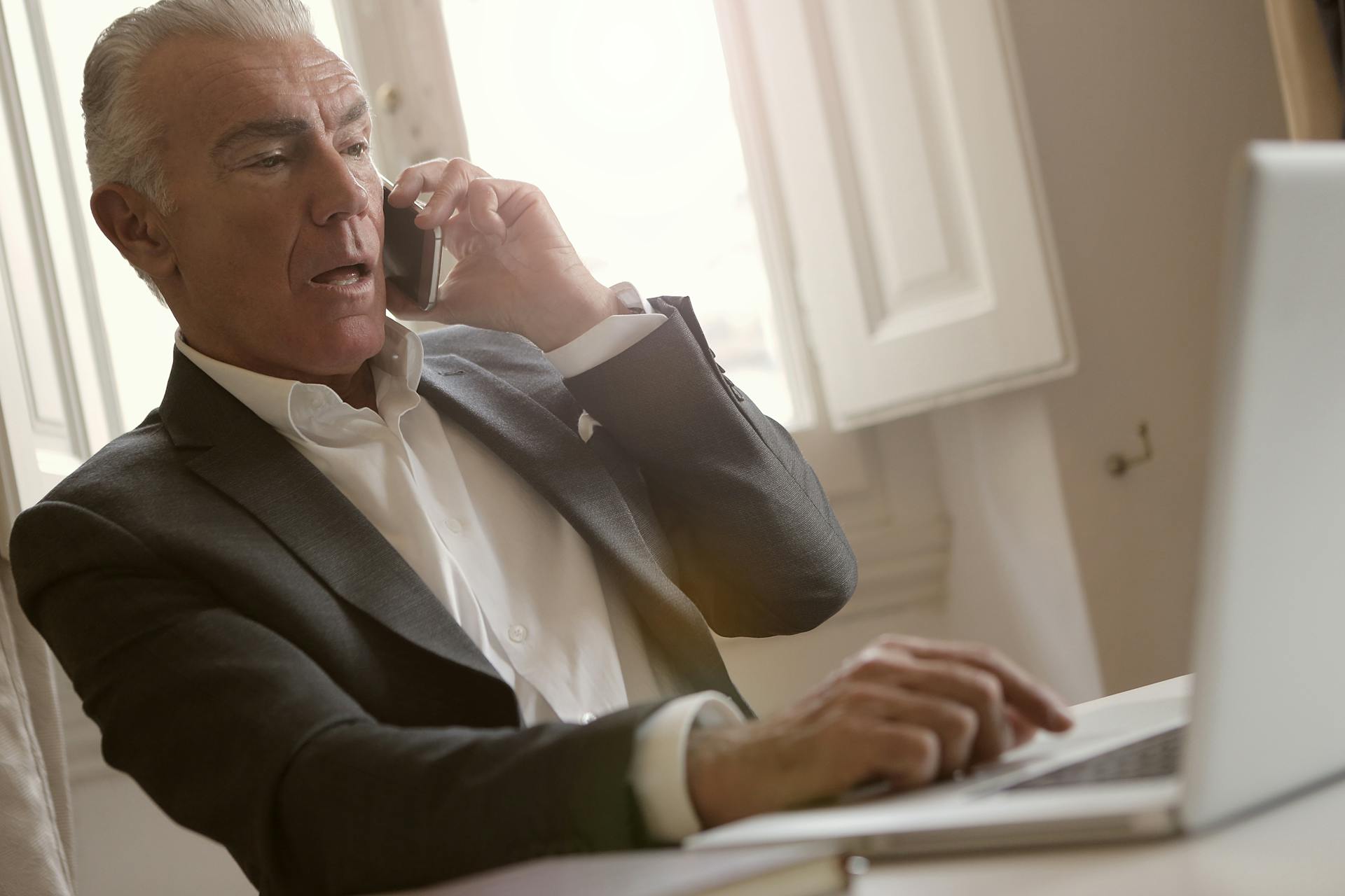 A worried man talking on the phone while using his laptop | Source: Pexels