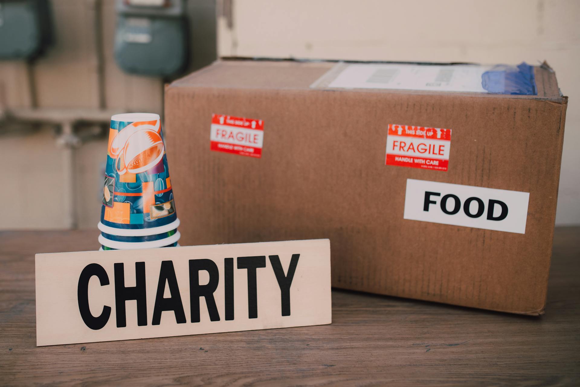 A cardboard box and a stack of paper cups beside a charity sign | Source: Pexels