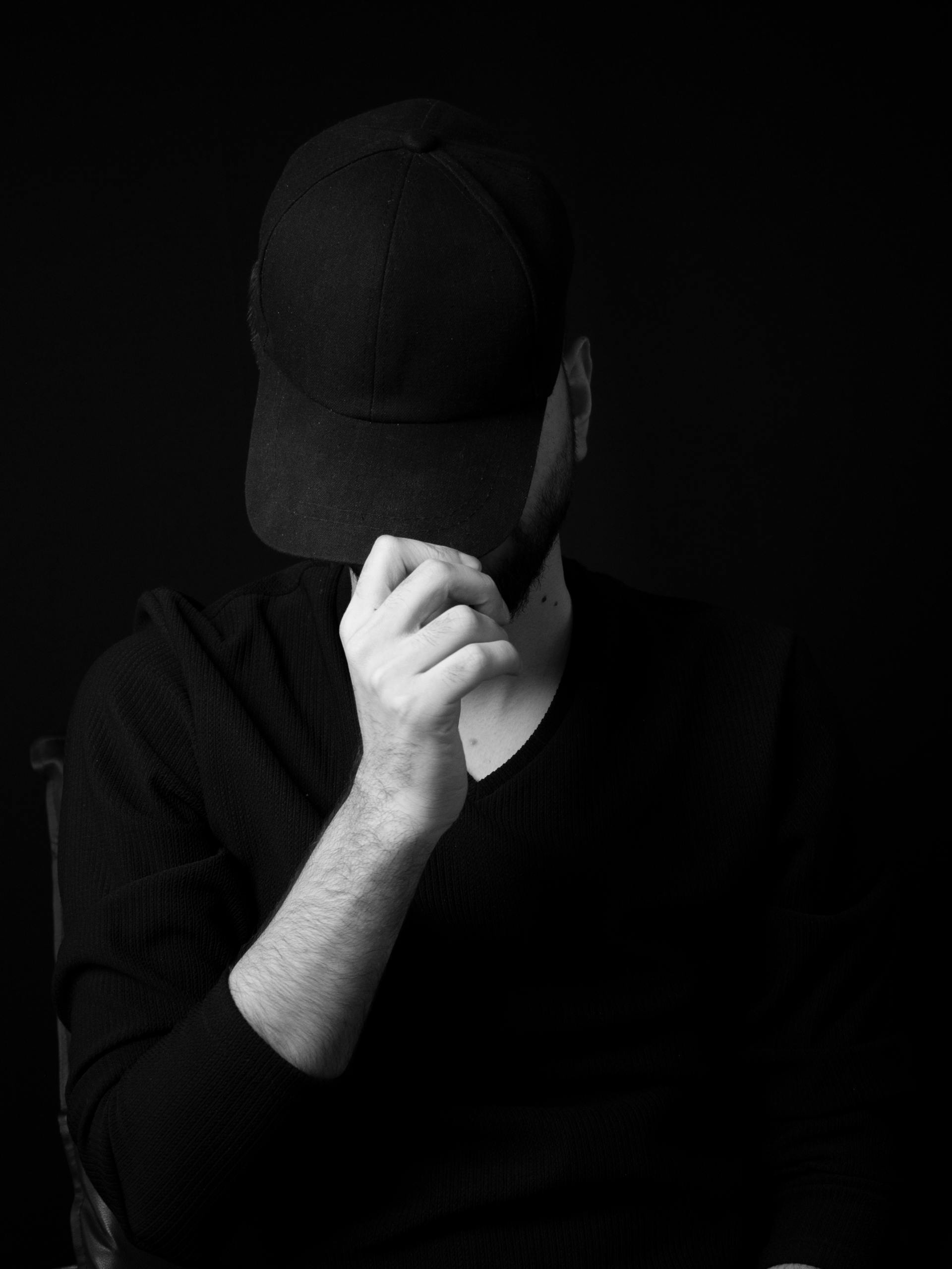 Grayscale photo of a man hiding his face with his cap | Source: Pexels