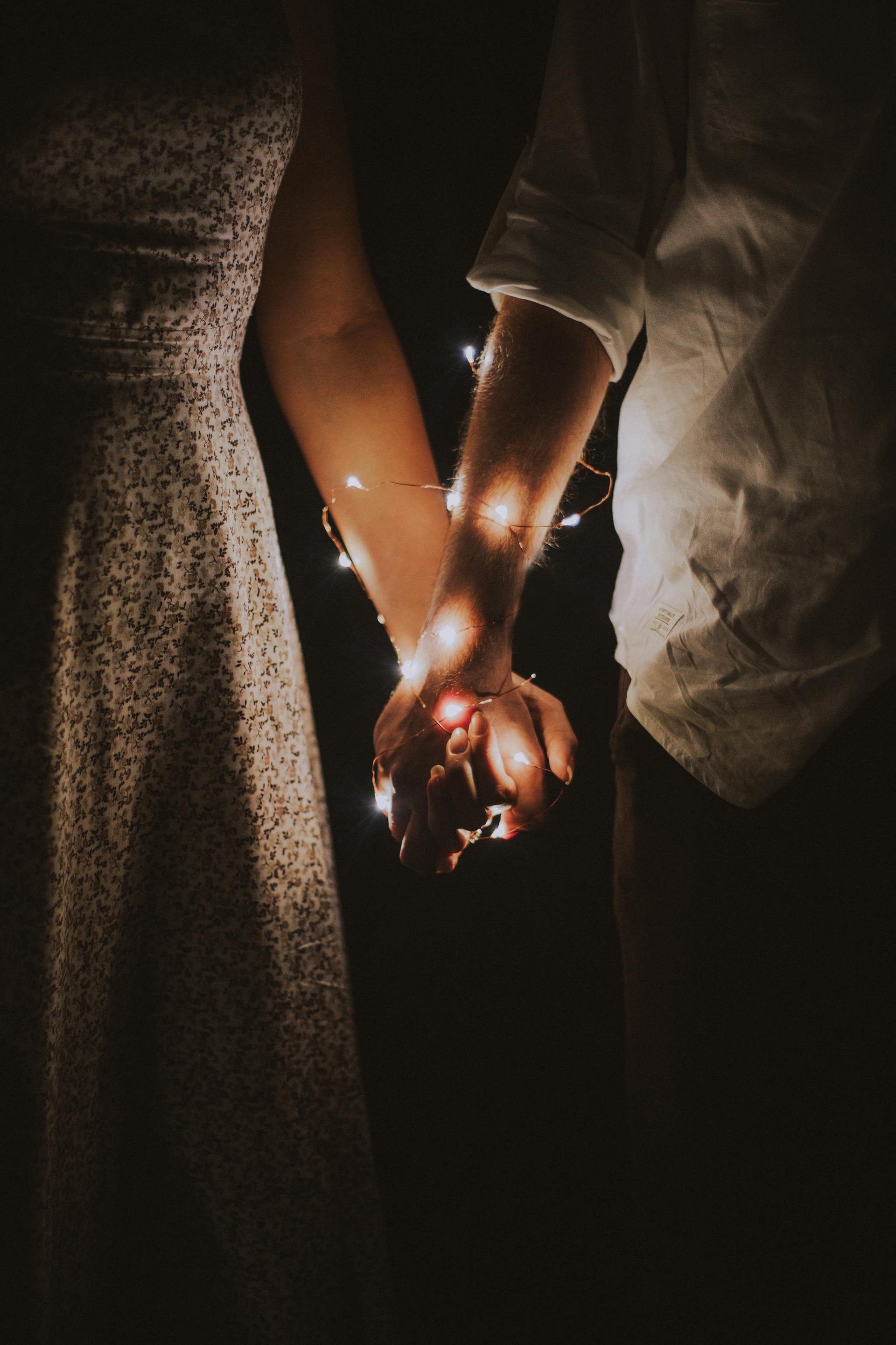 A couple holding hands wrapped with string lights | Source: Pexels