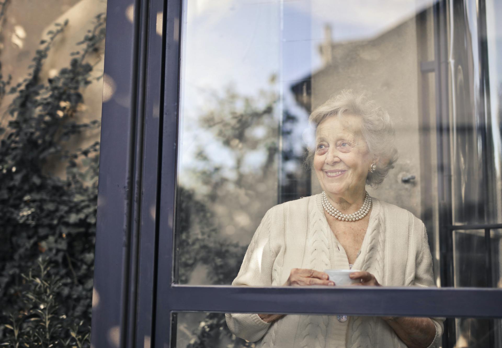 A smiling elderly lady holding her mug of tea and looking out the window | Source: Pexels