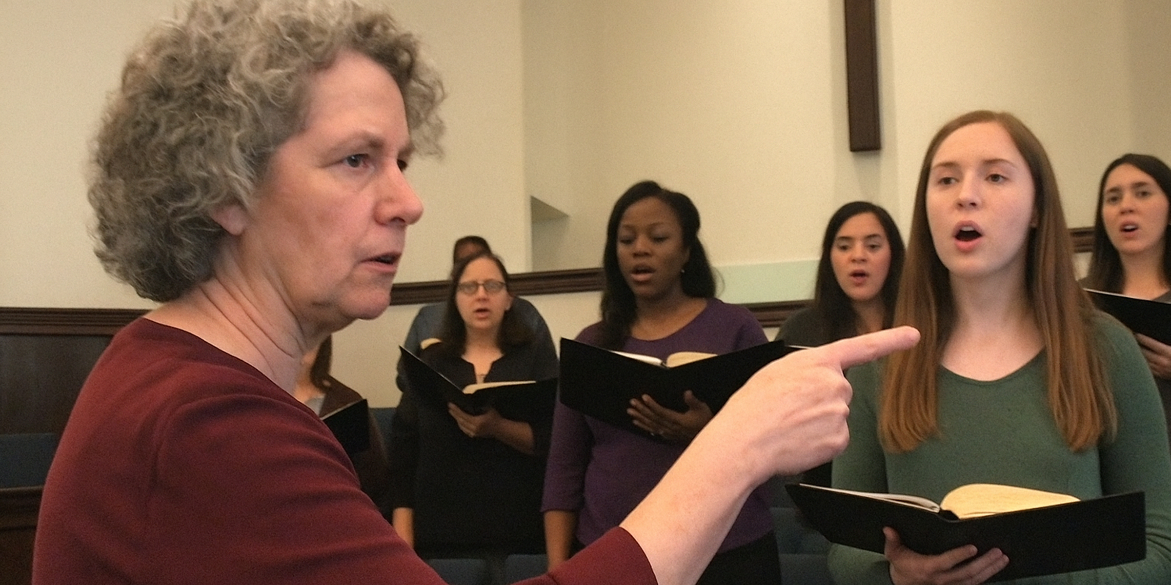 A stern older woman halts choir rehearsal, pointing sharply as stunned singers look on | Source: The Celebritist