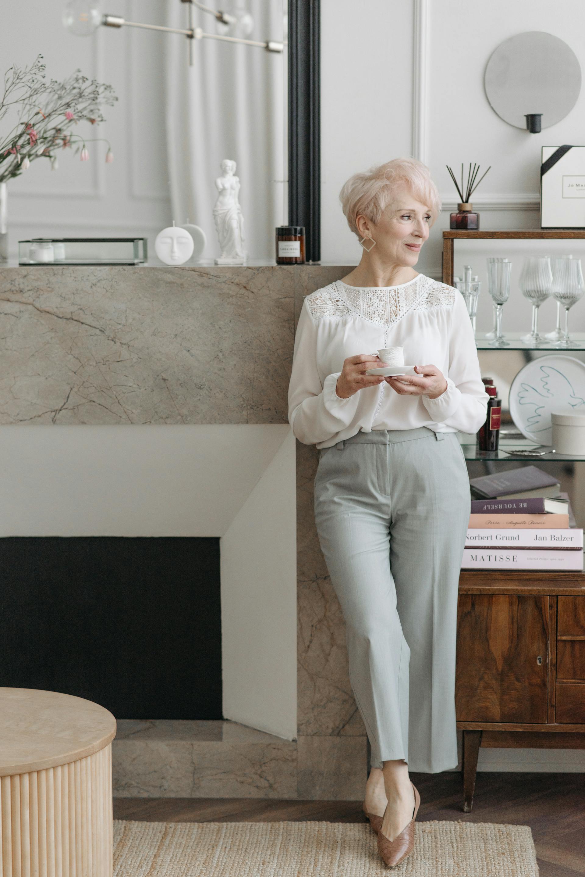 A senior woman standing beside a fireplace | Source: Pexels