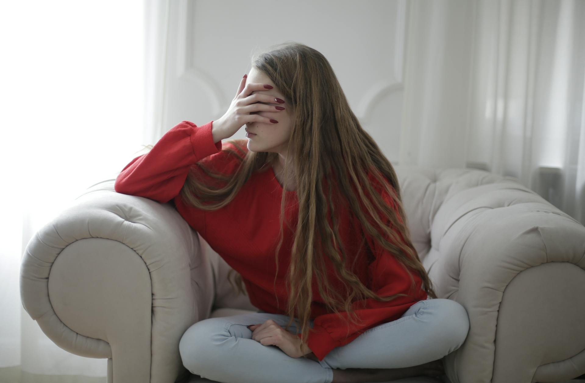 A woman sitting on an armchair and covering her eyes with her hands | Source: Pexels