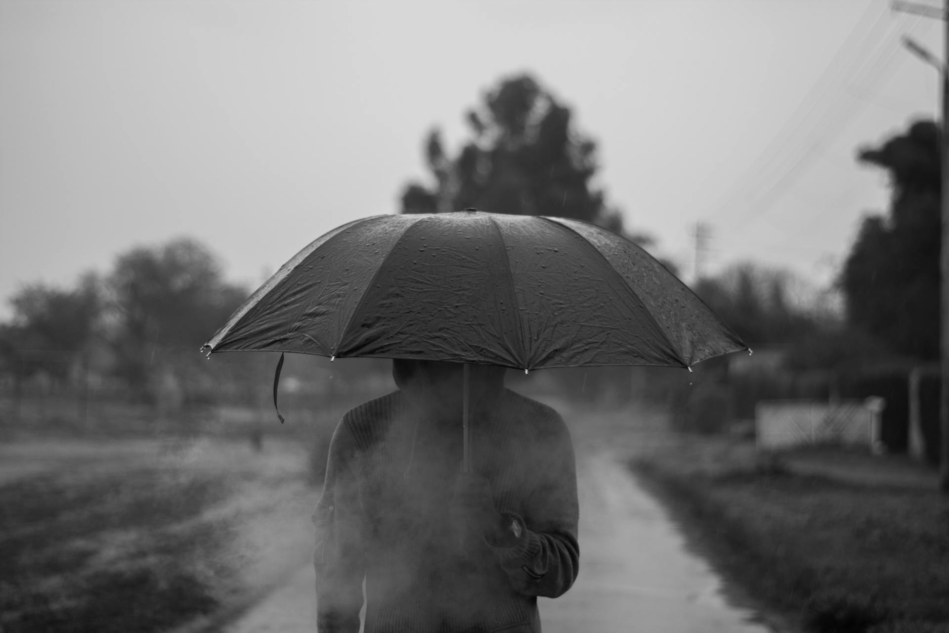 A grayscale photo of a person in a hoodie holding an umbrella | Source: Pexels