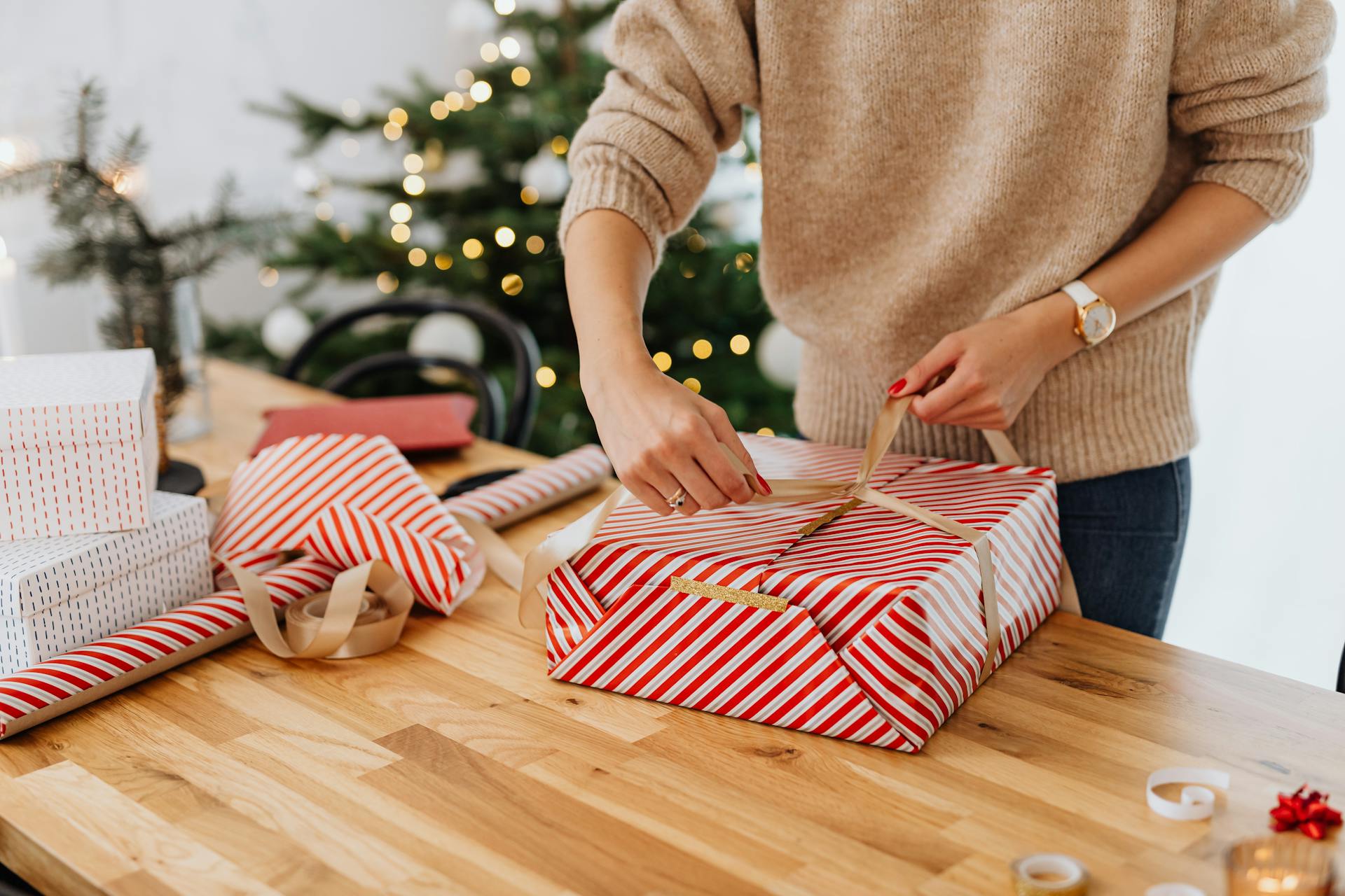 A woman wrapping a gift with a Christmas tree in the background | Source: Pexels