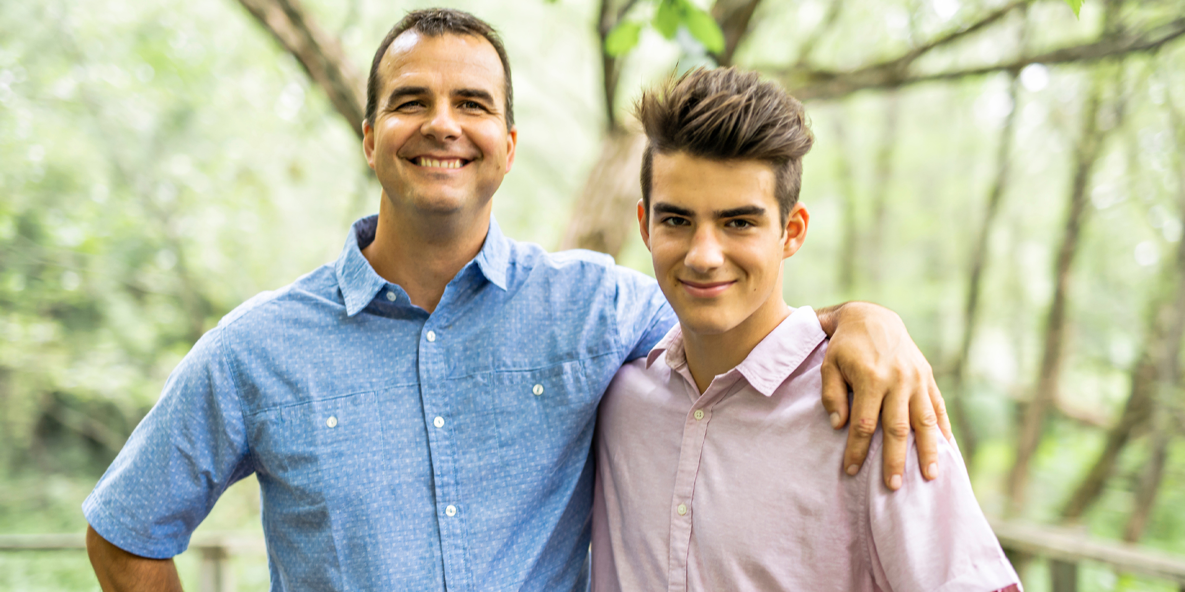 A smiling man and teenage boy posing together outdoors in a wooded area | Souce: Shutterstock