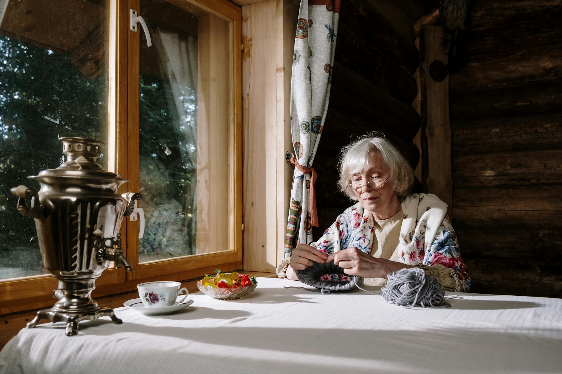 An older woman knitting beside a window | Source: Pexels