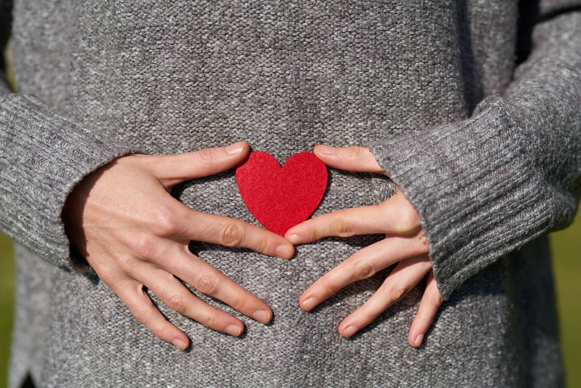 A woman holding a heart-shaped cutout close to her belly | Source: Pexels