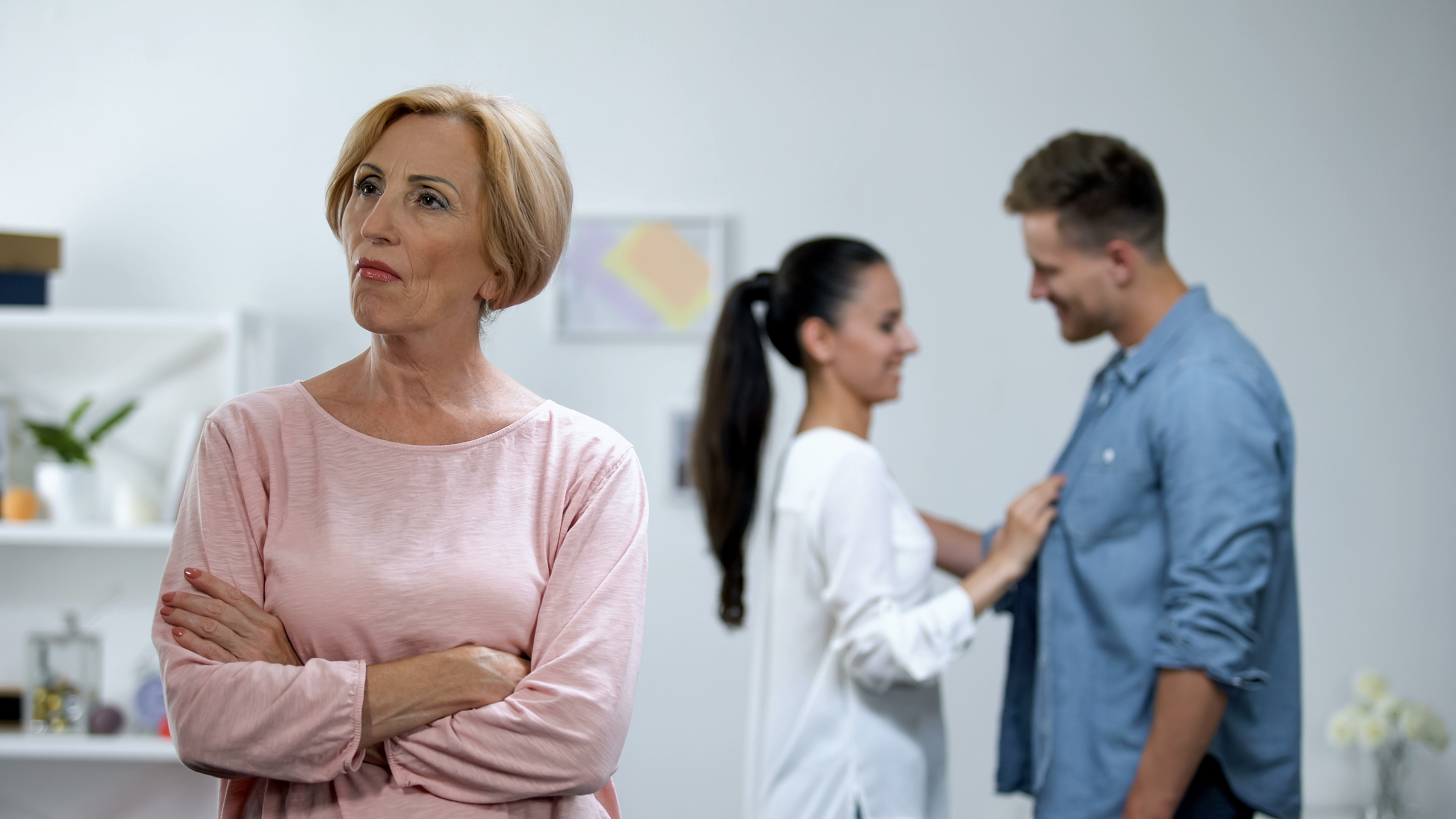 A mother-in-law standing with her arms crossed with her son and daughter-in-law appearing happy in the background | Source: Shutterstock