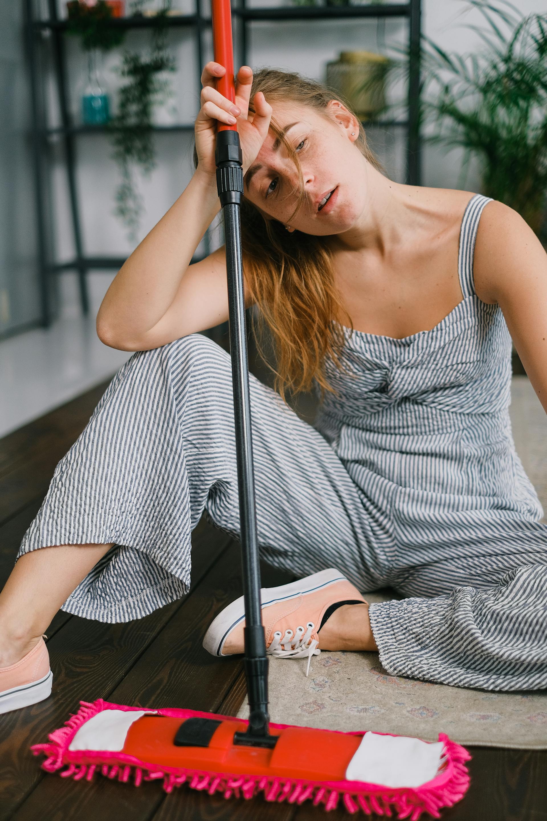 A tired woman with a mop sitting on a rug looking sideways | Source: Pexels