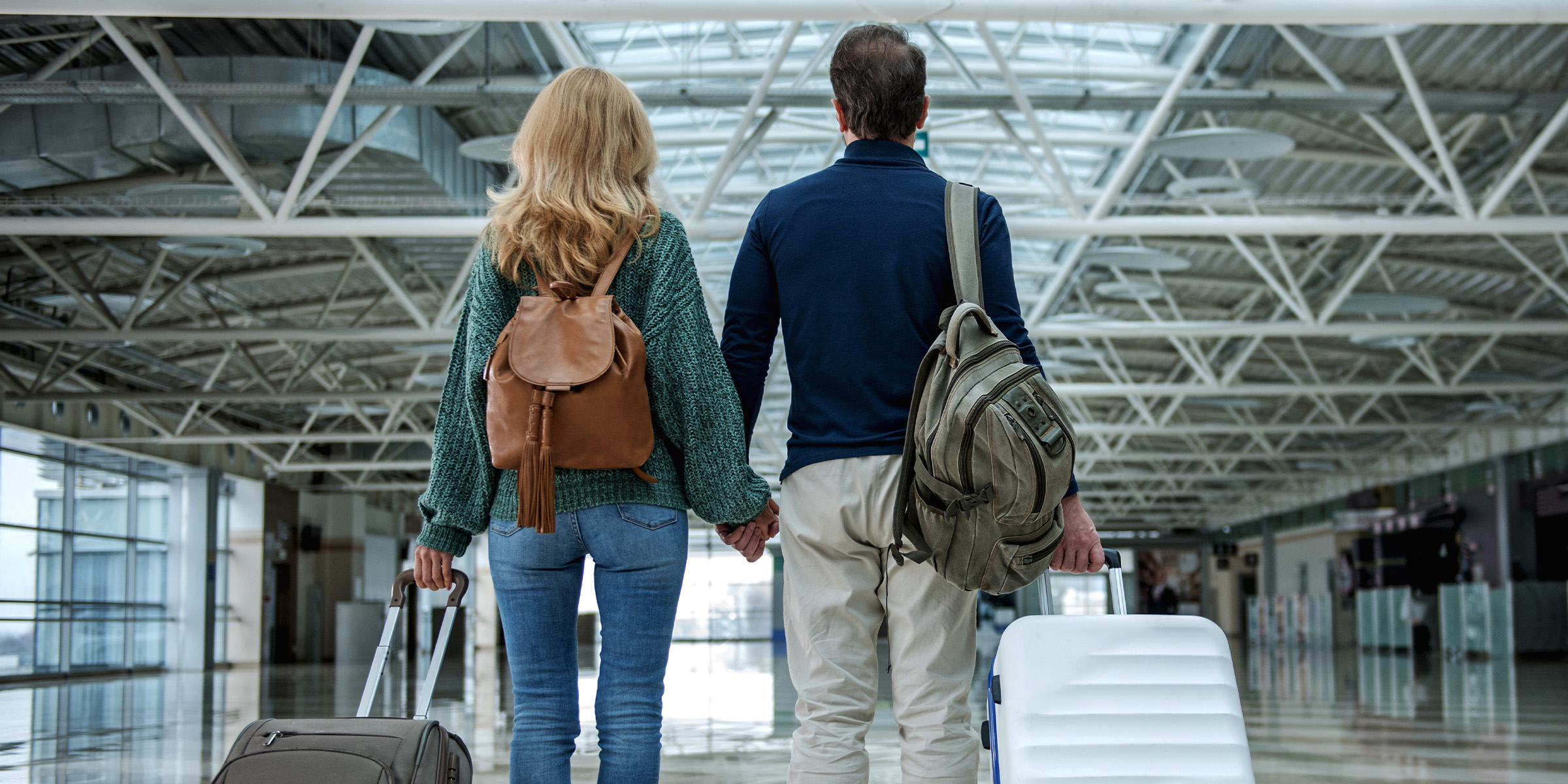 A couple standing hand in hand in an airport, each holding a suitcase | Source: Shutterstock