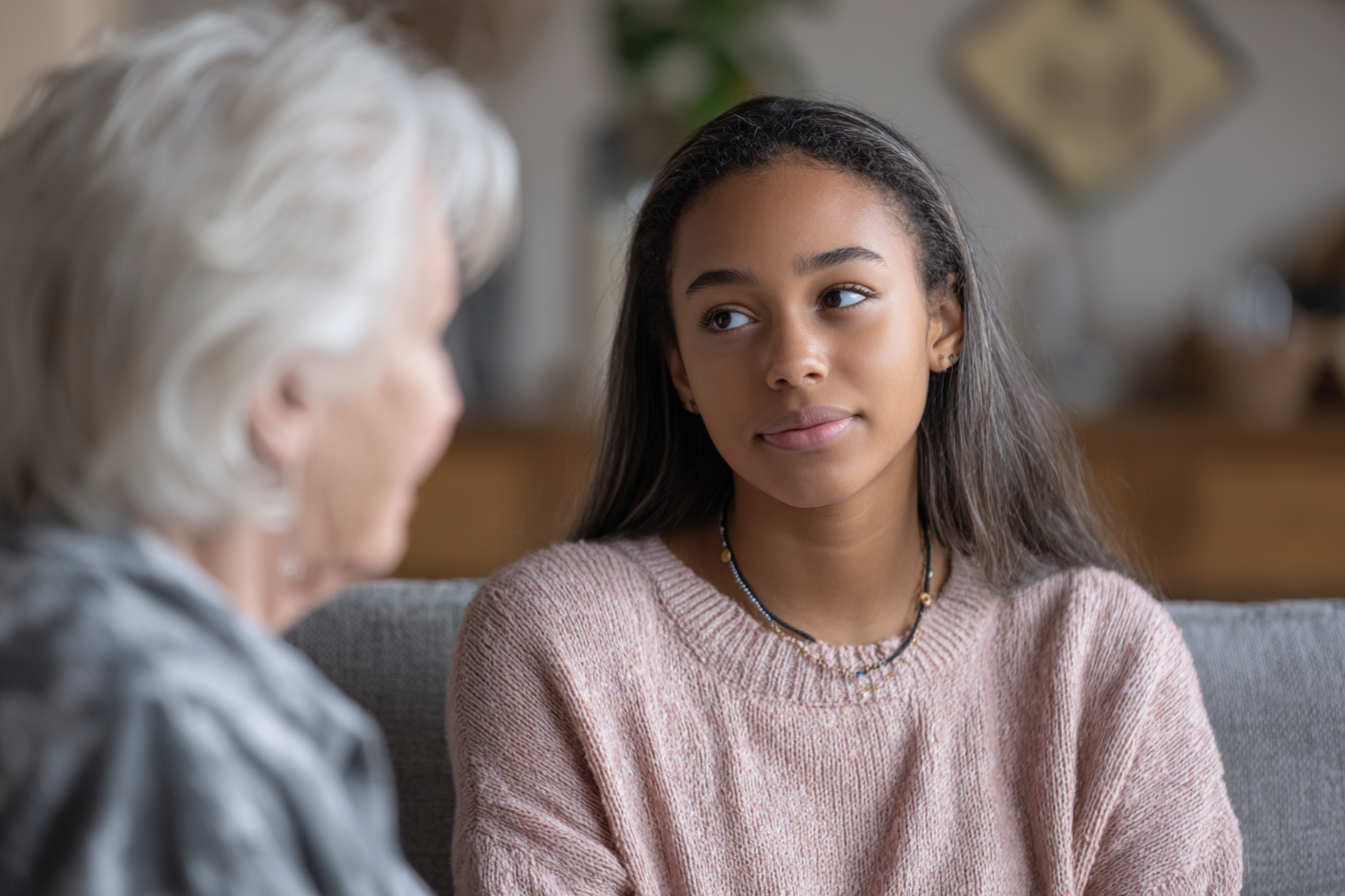 An older woman conversing with a teen girl in a living room | Source: Midjourney