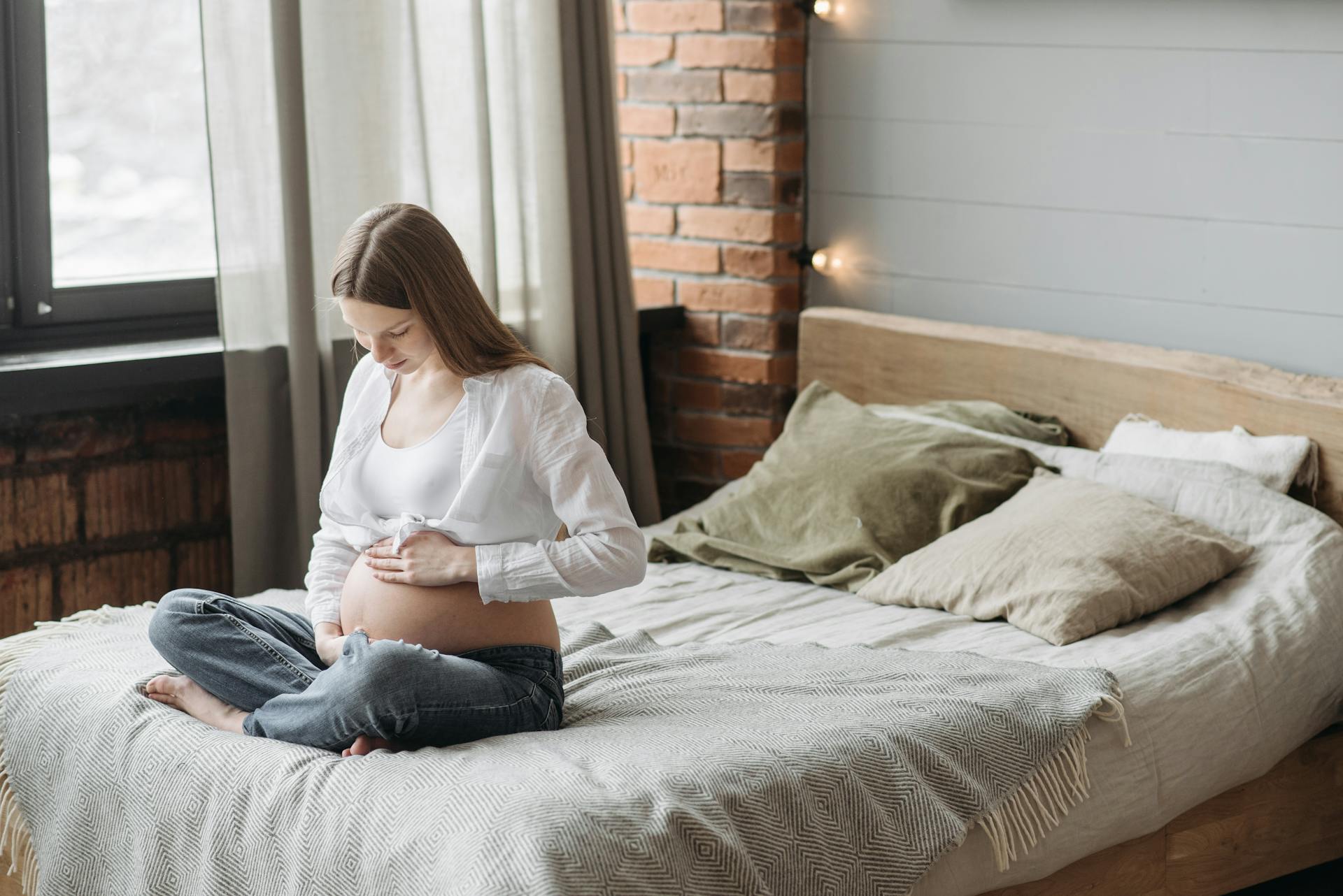 A pregnant woman sitting on the bed holding her belly | Source: Pexels