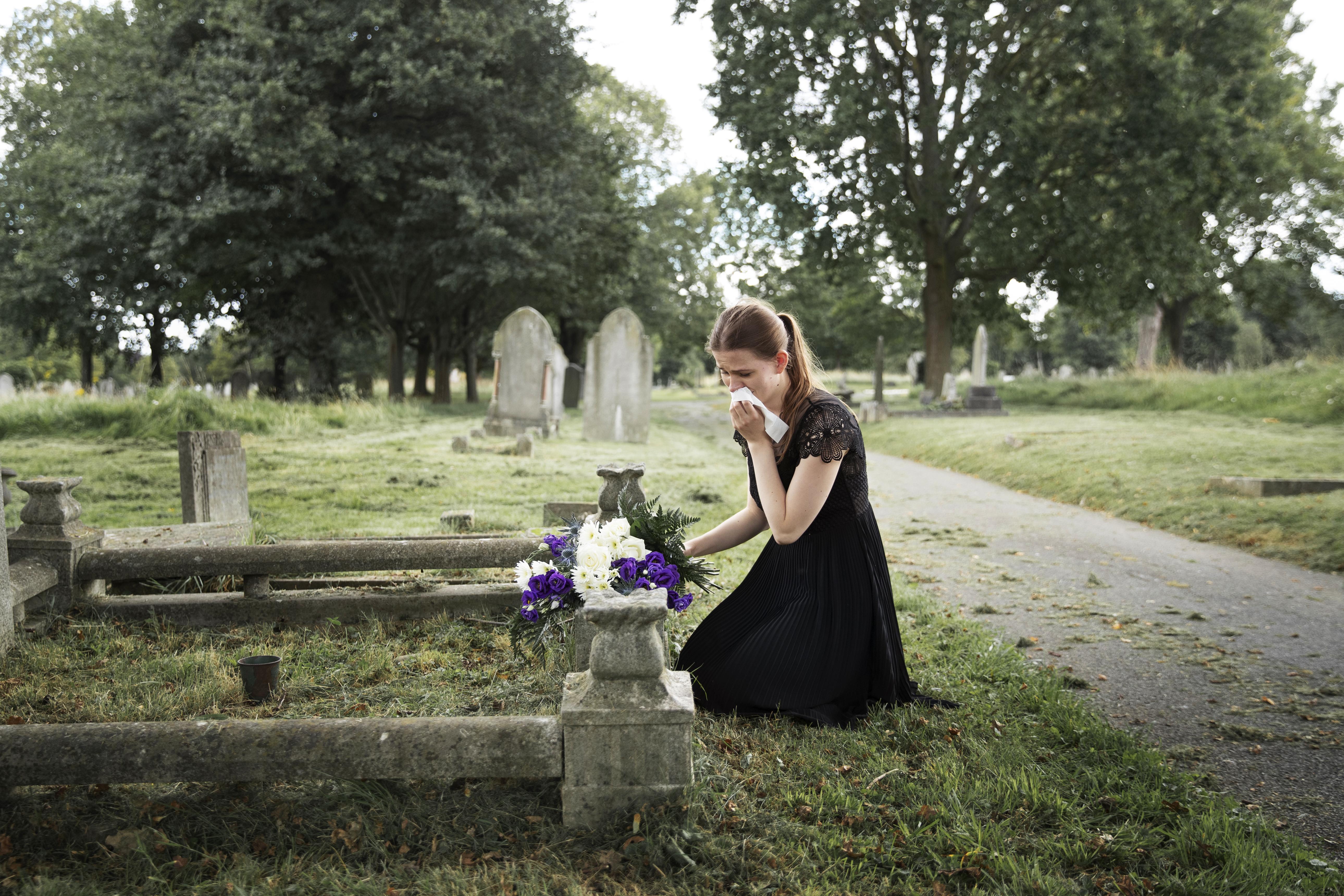 A grieving young woman mourning before a loved one's grave | Source: Freepik